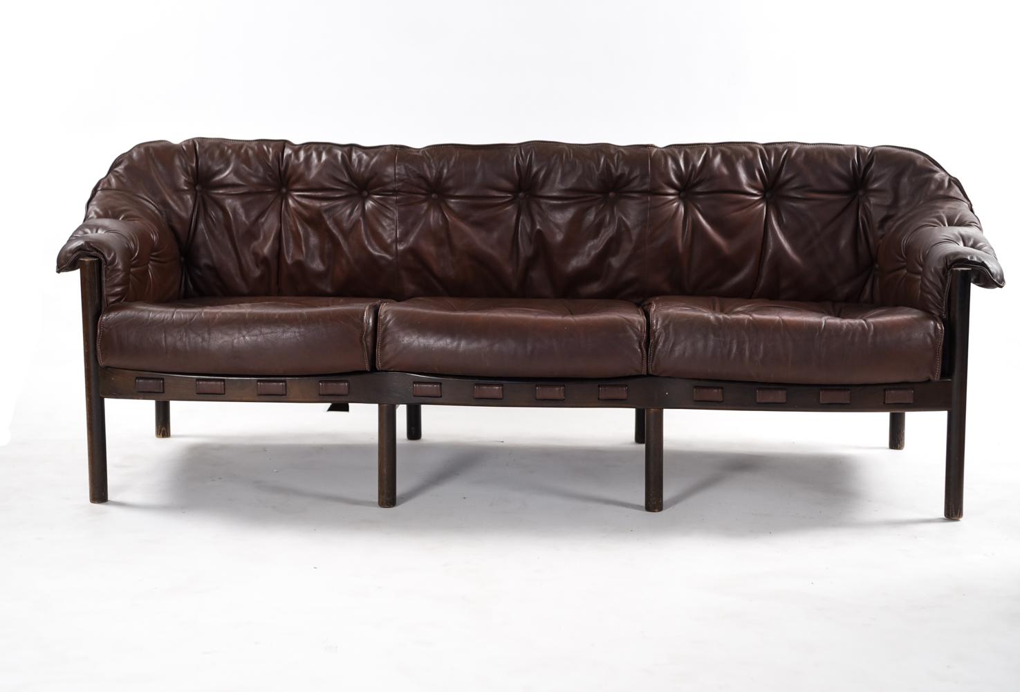 This midcentury three-seat sofa was designed by Arne Norrell for Coja, 1960s. Upholstered in a button tufted brown leather, displaying an attractive vintage patina. A well known, respected design in Scandinavian Modern furniture.