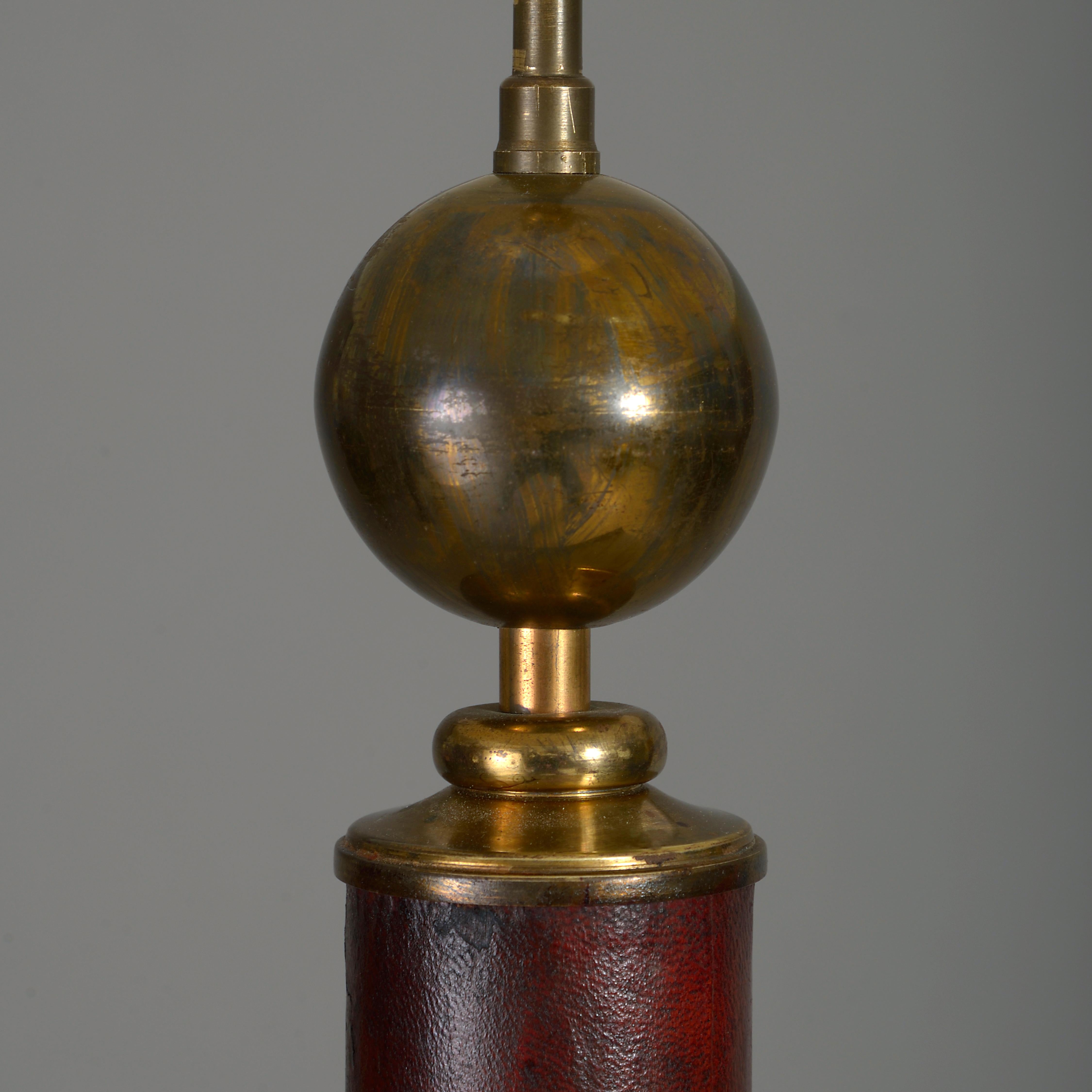 A mid-20th century standard lamp, the bulb holder supported upon a brass sphere set on a leather covered column stem, terminating in a concave triform base with brass feet.



 