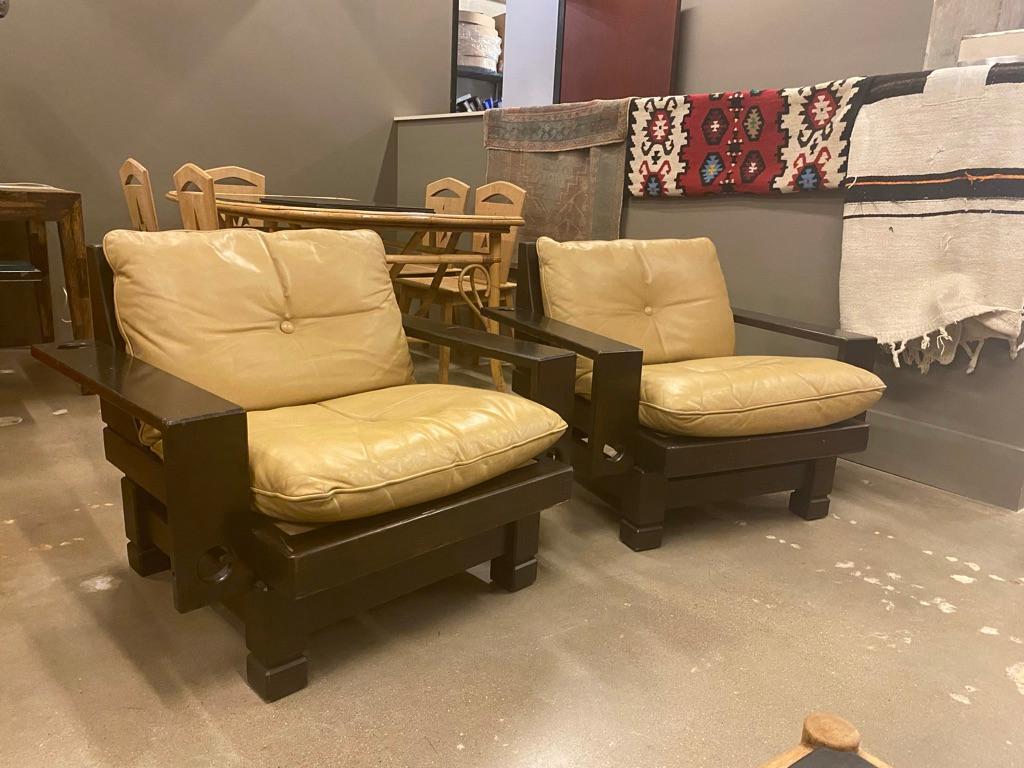 Vintage European pair of lounge chairs. Dark stained sculptural wood frames with khaki or tan leather seats and backs. Mid-Century Modern to Brutalist styling. Cushions are reversible and very comfortable. Possibly a combination of foam and down.