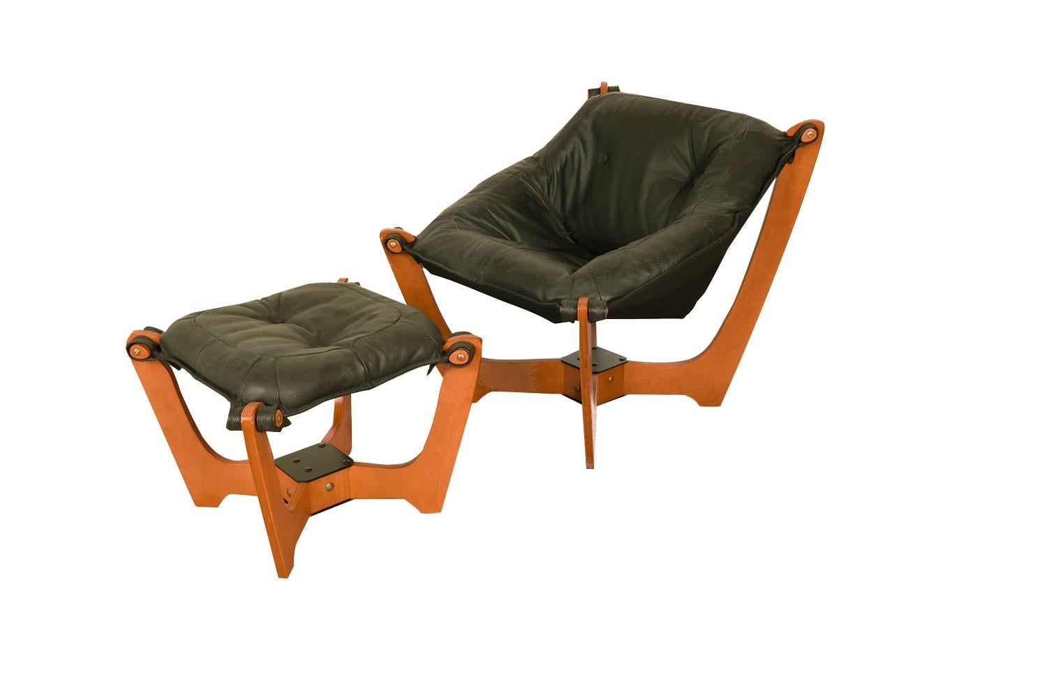 A beautiful Mid-Century Modern, stylish leather Luna Sling lounge chair and ottoman circa 1970s product by Hjellegjerde group of Norway. Features rich, soft, black leather upholstery, in a light color wood frame. The sculptural frame with low back