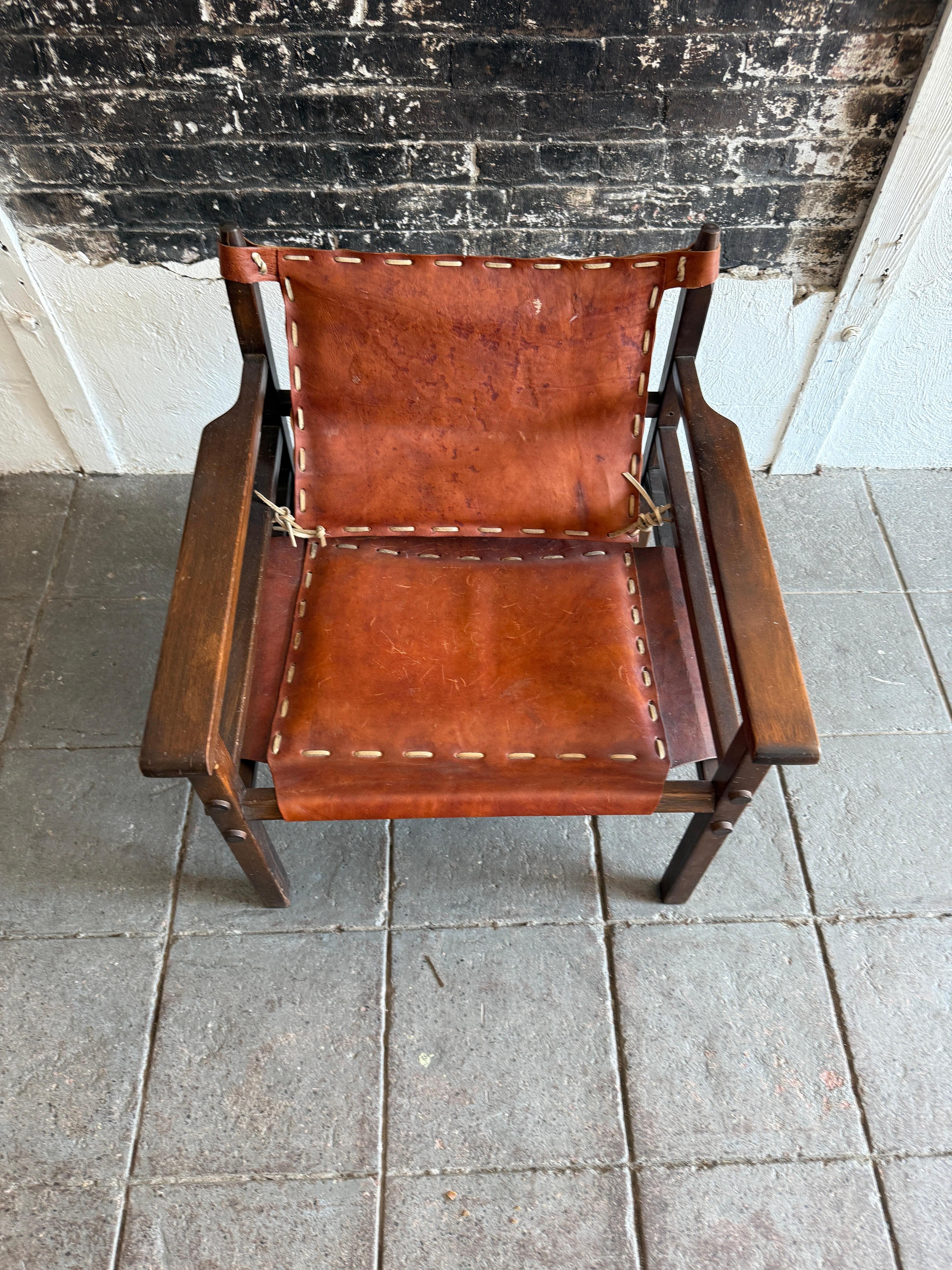Sillón safari moderno escandinavo al estilo de Arne Norell. Precioso asiento de cabestrillo de cuero marrón rojizo cálido envejecido, con pátina y mucho carácter. Tiene un robusto armazón de madera dura con asientos de cuero tejido. Buen estado