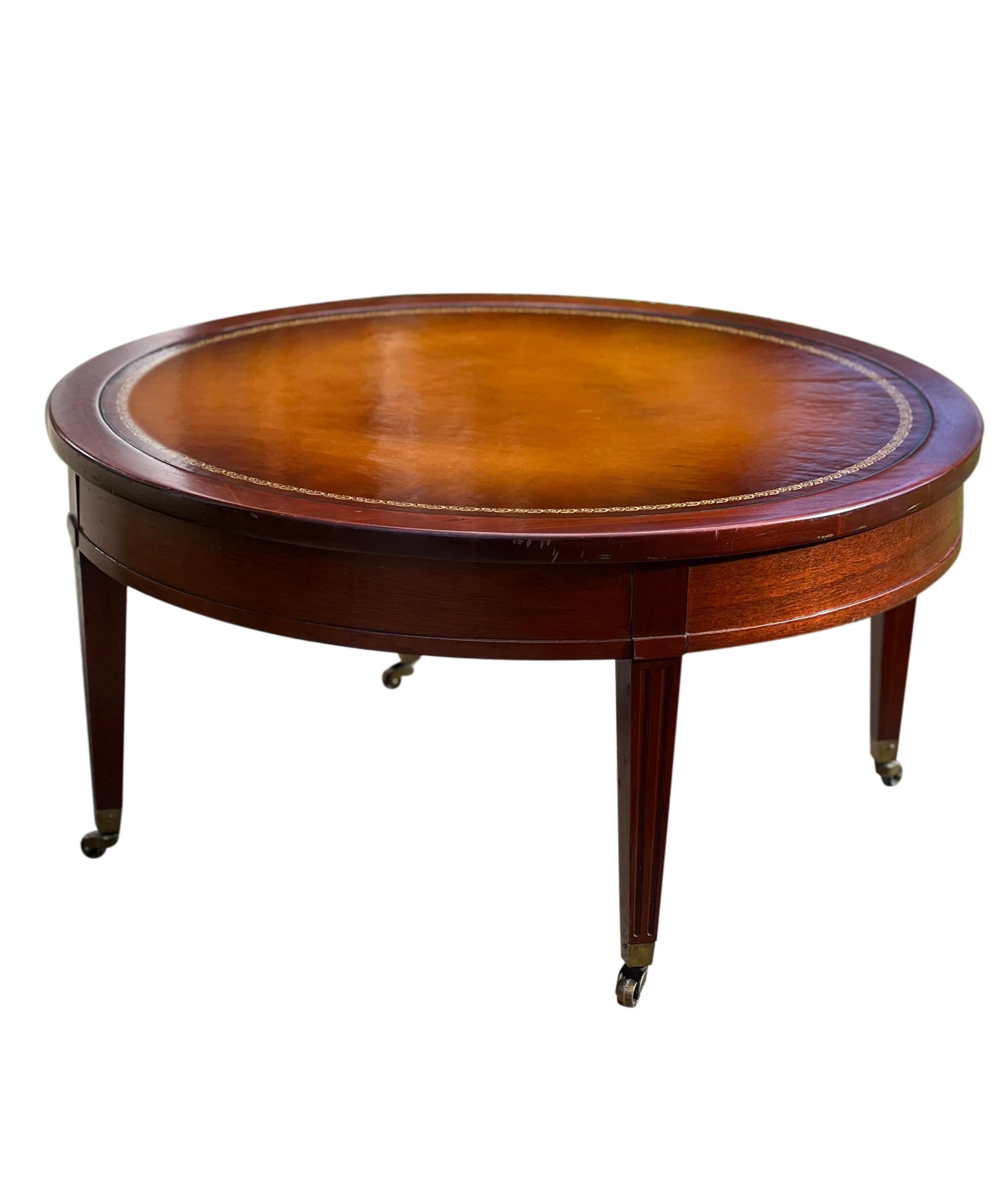 Handsome mid-century round leather top mahogany coffee table on casters by Mersman. The table features a classic period style with a beautiful inlaid leather top and gold stenciling. An elegant, well-crafted piece in very good vintage condition.