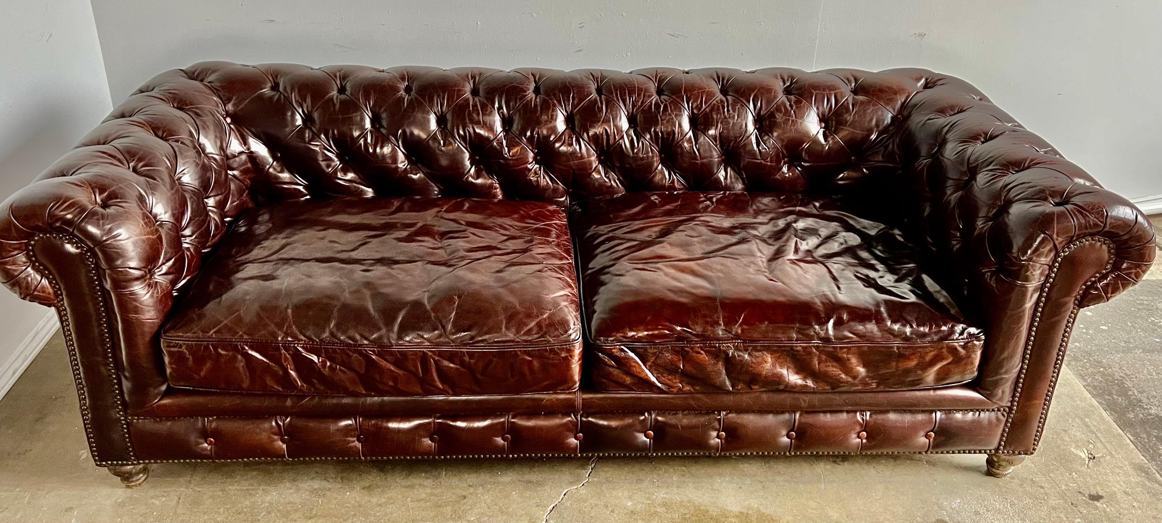 Handsome English leather tufted sofa with tight tufted back and two loose seat cushions. The sofa is beautifully detailed with brass nailhead trim. Wonderfully worn with no tears of holes in the leather.