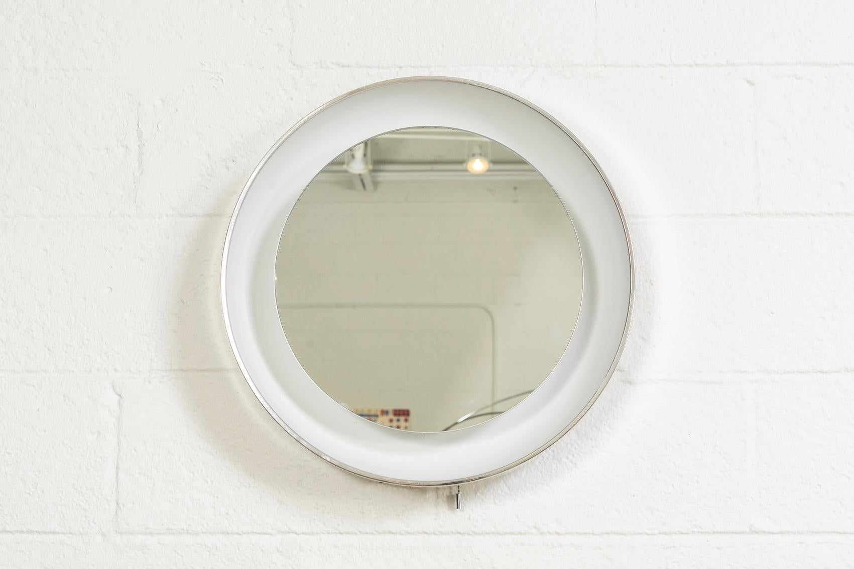 This Mid-Century Modern Lightolier illuminated wall or vanity mirror is circa 1970 and features a large plastic frame with reflective white interior and polished aluminum outer edge. The original 15” mirror glass floats in the centre of the frame.