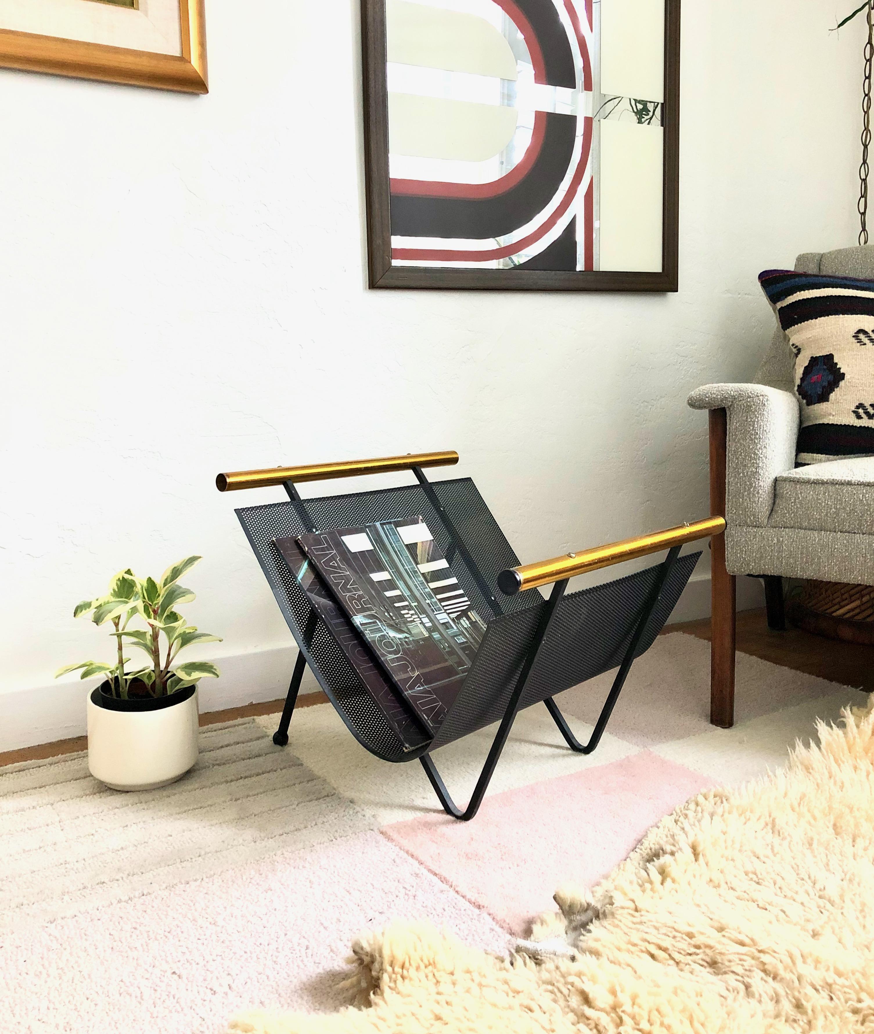 A mid century fireplace log holder designed by Gene Tepper for Smith Tepper Sundberg. Great atomic design, featuring a curved sheet of perforated black metal and bent iron legs with two gold toned handles on either side. Can also be used as a