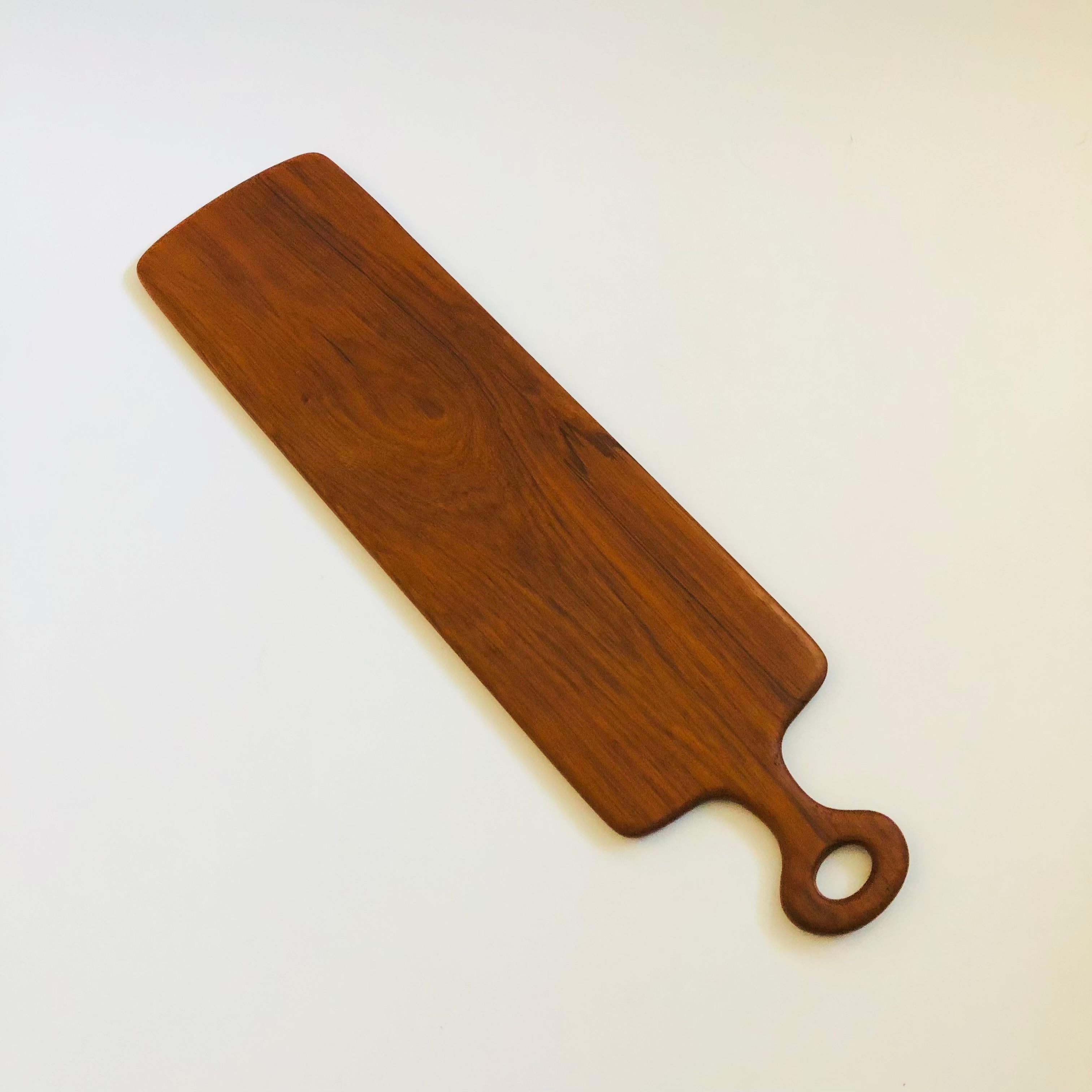 Una tabla de cortar vintage de pala larga de mediados de siglo. De madera de teca con un asa redondeada en un lado. Fabricado en Tailandia.

