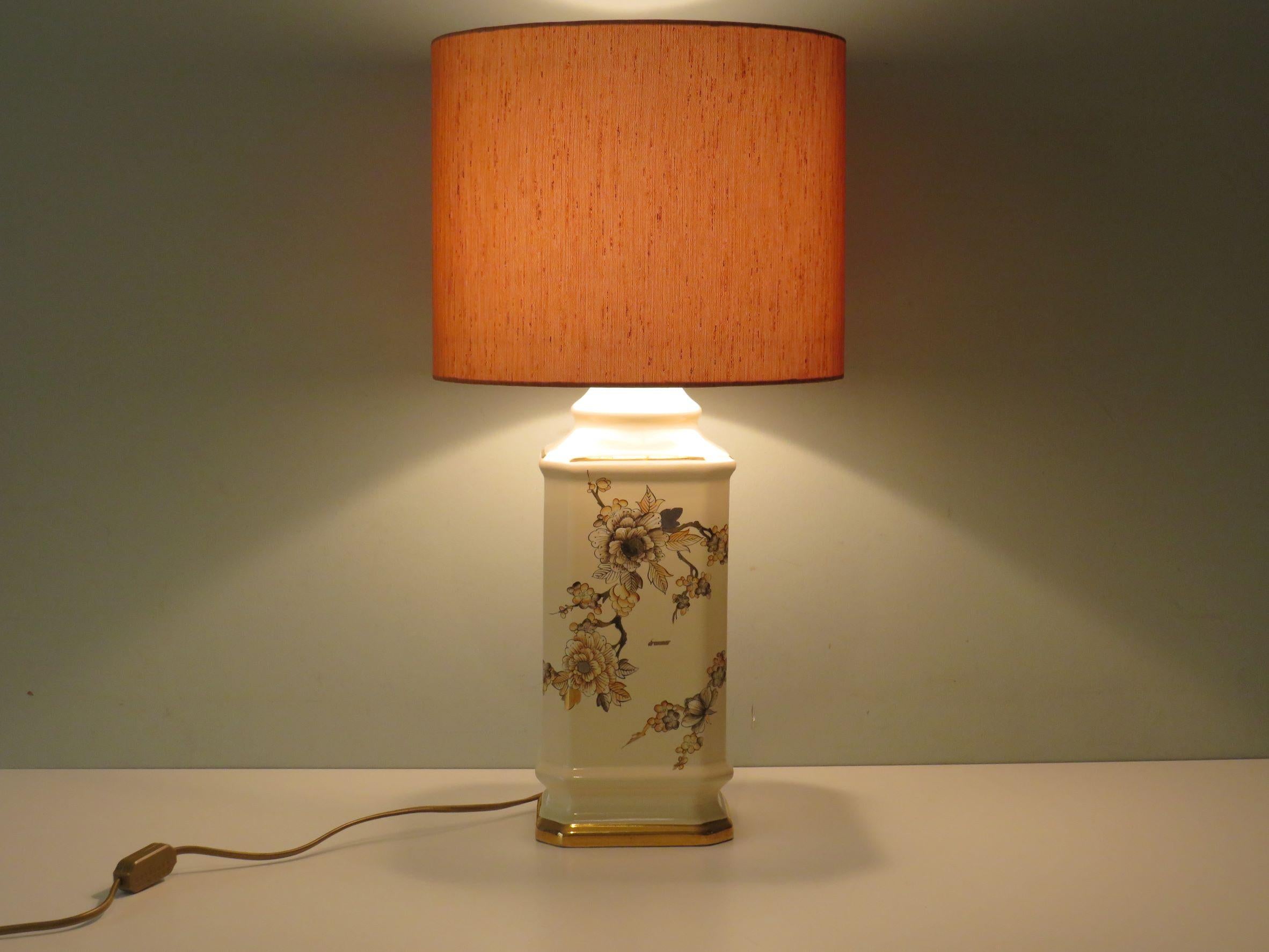 Pagoda-shaped, cream-coloured lamp base with floral pattern in pink and gold-coloured tones. The new, custom made lampshade is made of orange-gold-brown structured fabric. The lamp is equipped with 1 E 27 fitting and a gold-coloured cord with a