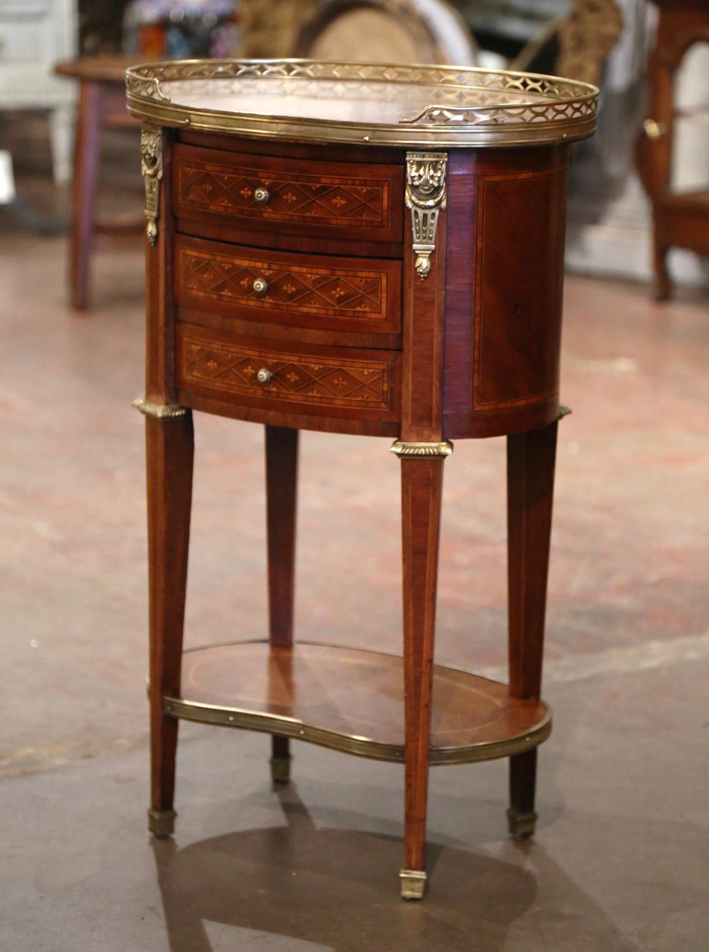 Crafted in France circa 1950 and built of walnut, the oval table sits on four tapered legs decorated with brass mounts at the shoulders, ending with bronze caps over feet. The chest features detailed marquetry work around the apron, and is further