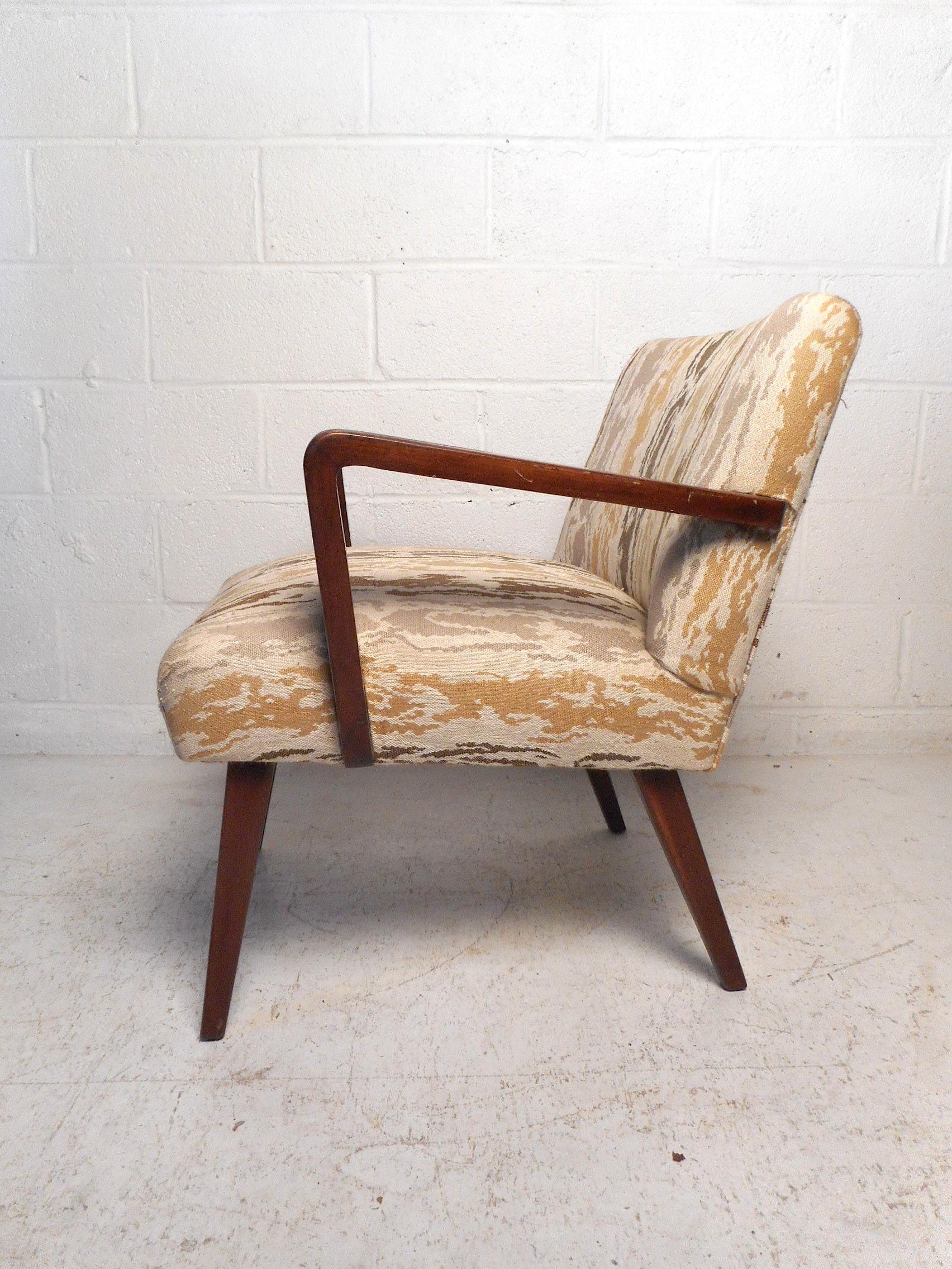 This impressive Mid-Century Modern lounge chair features a sturdy finished walnut frame, comfortable seating covered with a stylish vintage upholstery, sleekly splayed and tapered legs, and flared armrests giving the piece a remarkable visual