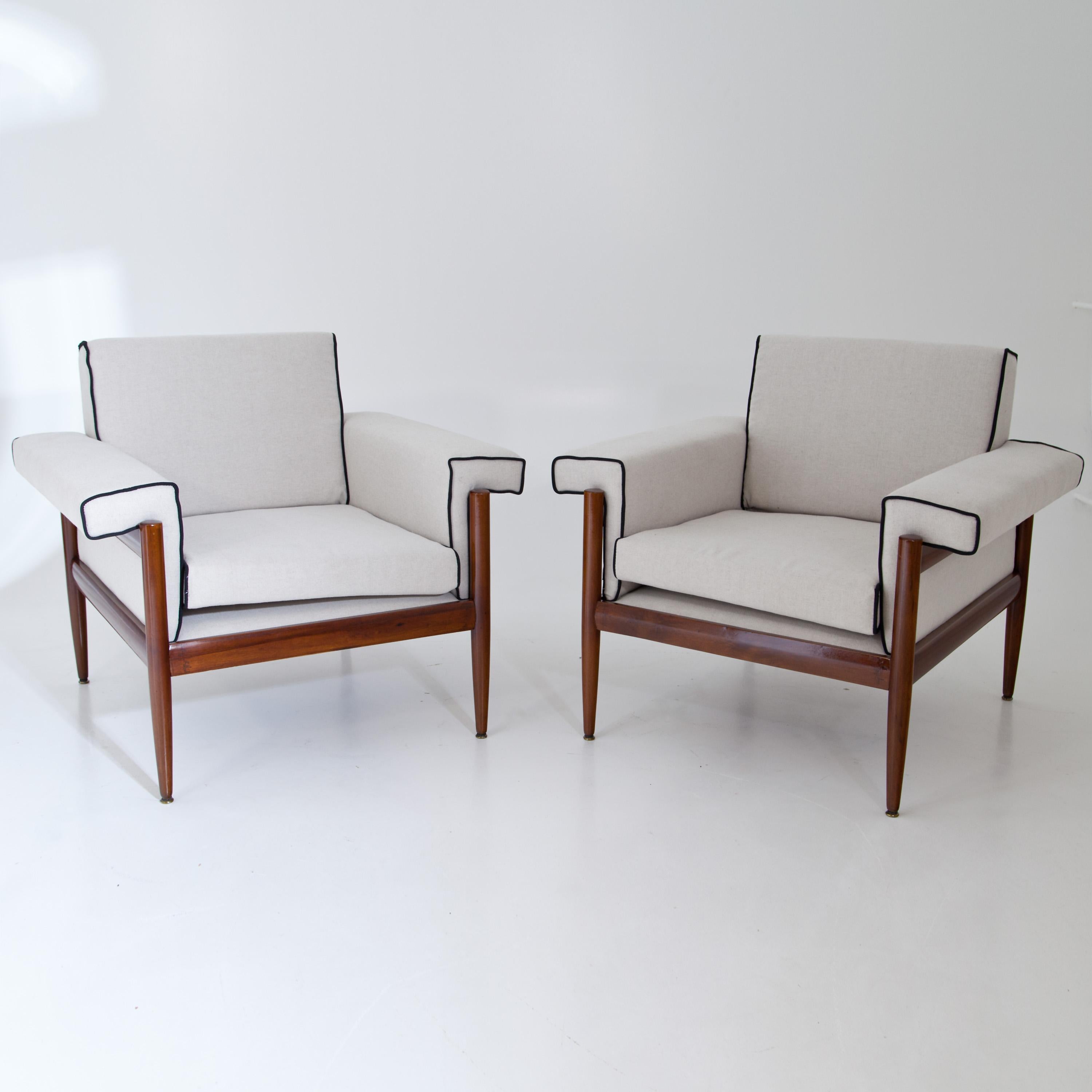 Pair of midcentury armchairs on conical legs and straight frames. The upholstery was newly covered with a white woven fabric with black piping.