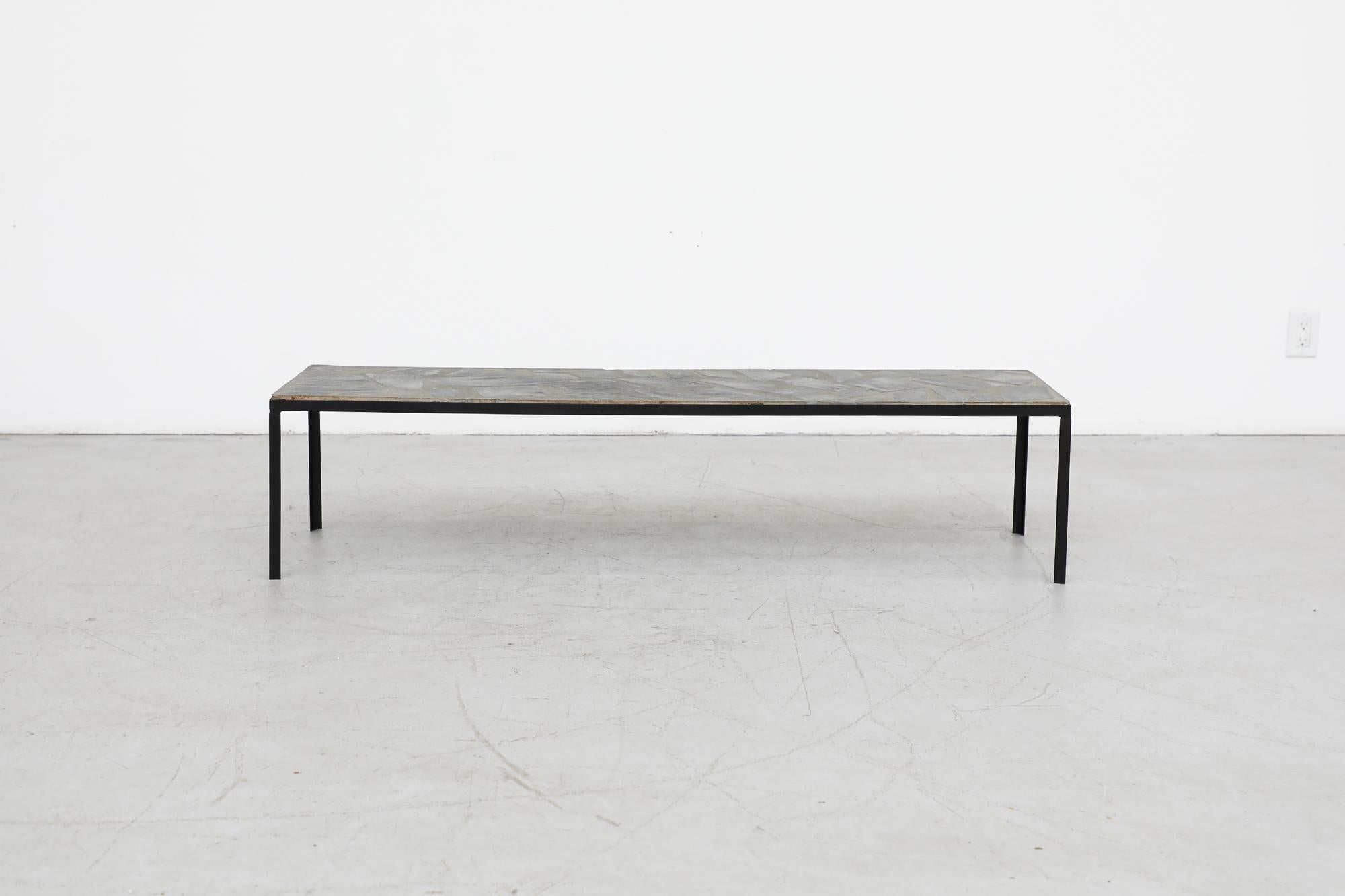 Extra long and low natural stone mosaic table with black industrial metal frame. In original condition with visible wear consistent with its age and use.