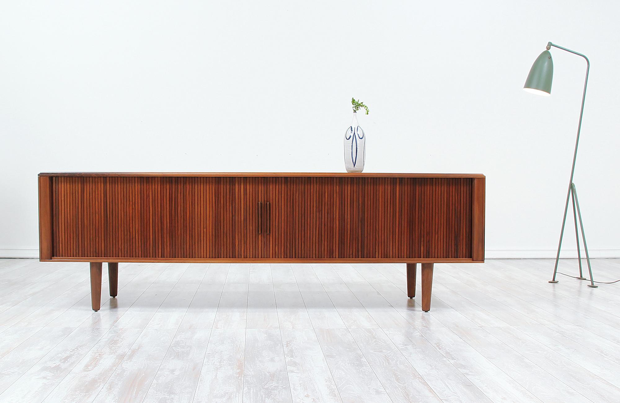 Mid-Century Modern credenza designed and manufactured in the United States by Barzilay circa 1960s. Low in profile and ample in space, this beautifully refinished walnut storage unit features two tambour doors that are accented with inconspicuously