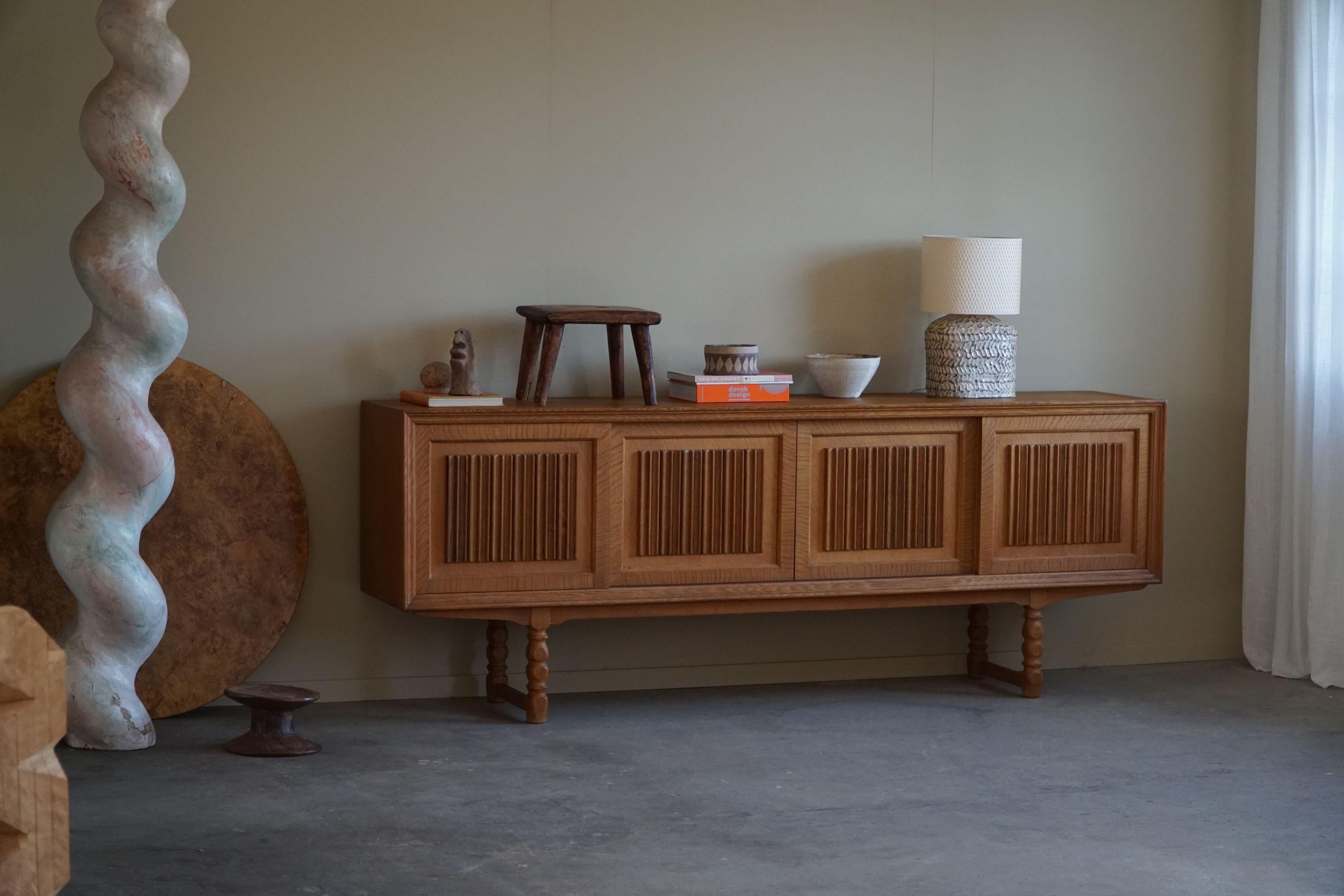 A sculptural low rectangular classic sideboard / cabinet in oak with plenty of storage and a nice carved front design. Made by a Danish cabinetmaker in the 1960s. 
Four sliding doors, inside storage and drawers.
This piece is in a good vintage
