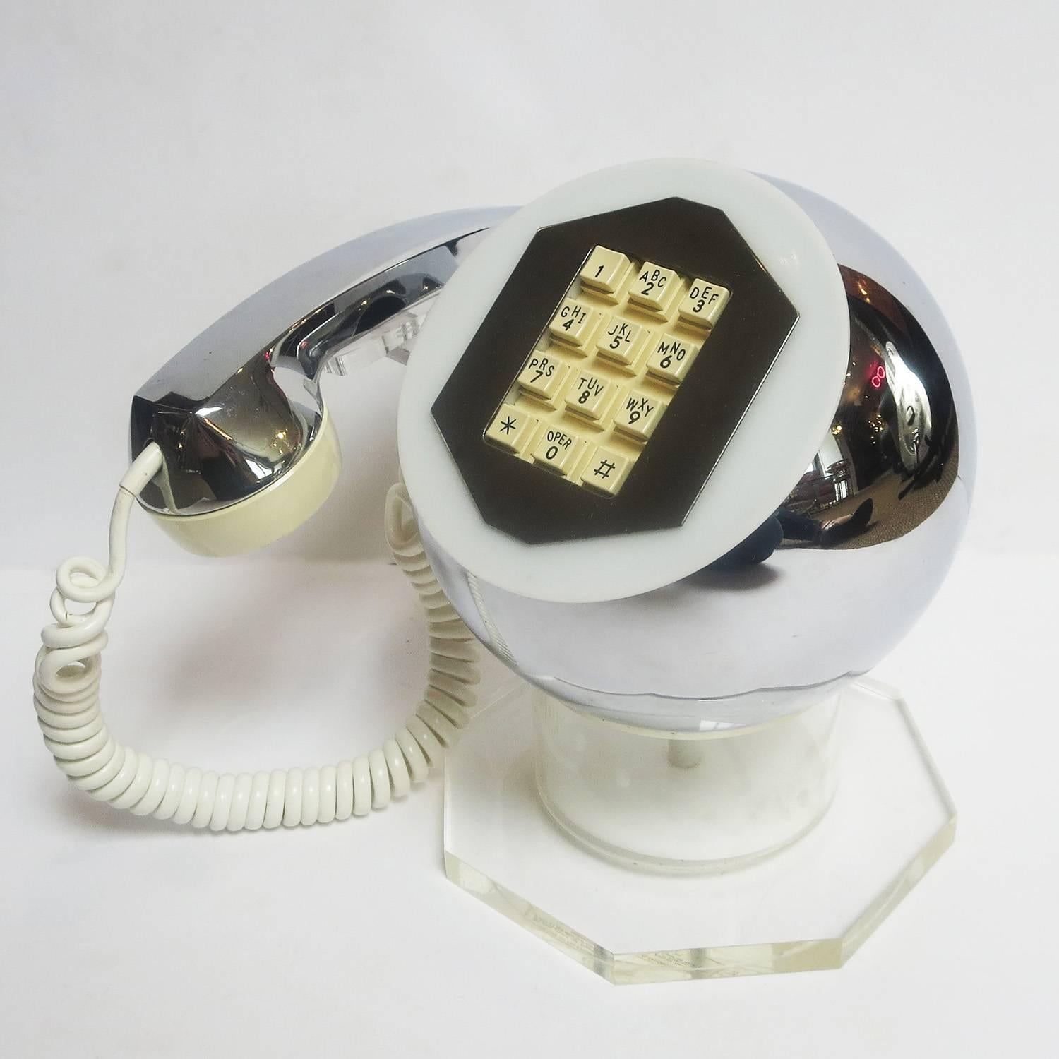 Create the ultimate statement with this wonderful Mod phone! The body of the telephone is a chrome ball, supported by a clear Lucite column and thick octagon base. The handset is a combination of chrome and plastic, and nests on a clear Lucite arm.