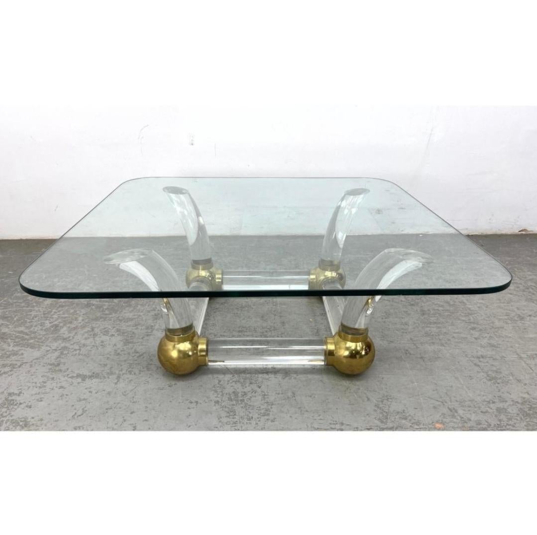 Table de cocktail sexy, sculpturale et glamour avec un cadre épais et incurvé en Lucite et laiton, et un plateau en verre de plus d'un demi-pouce d'épaisseur. 

Cet article peut être vu en personne aux Berkshire Galleries de Great Barrington