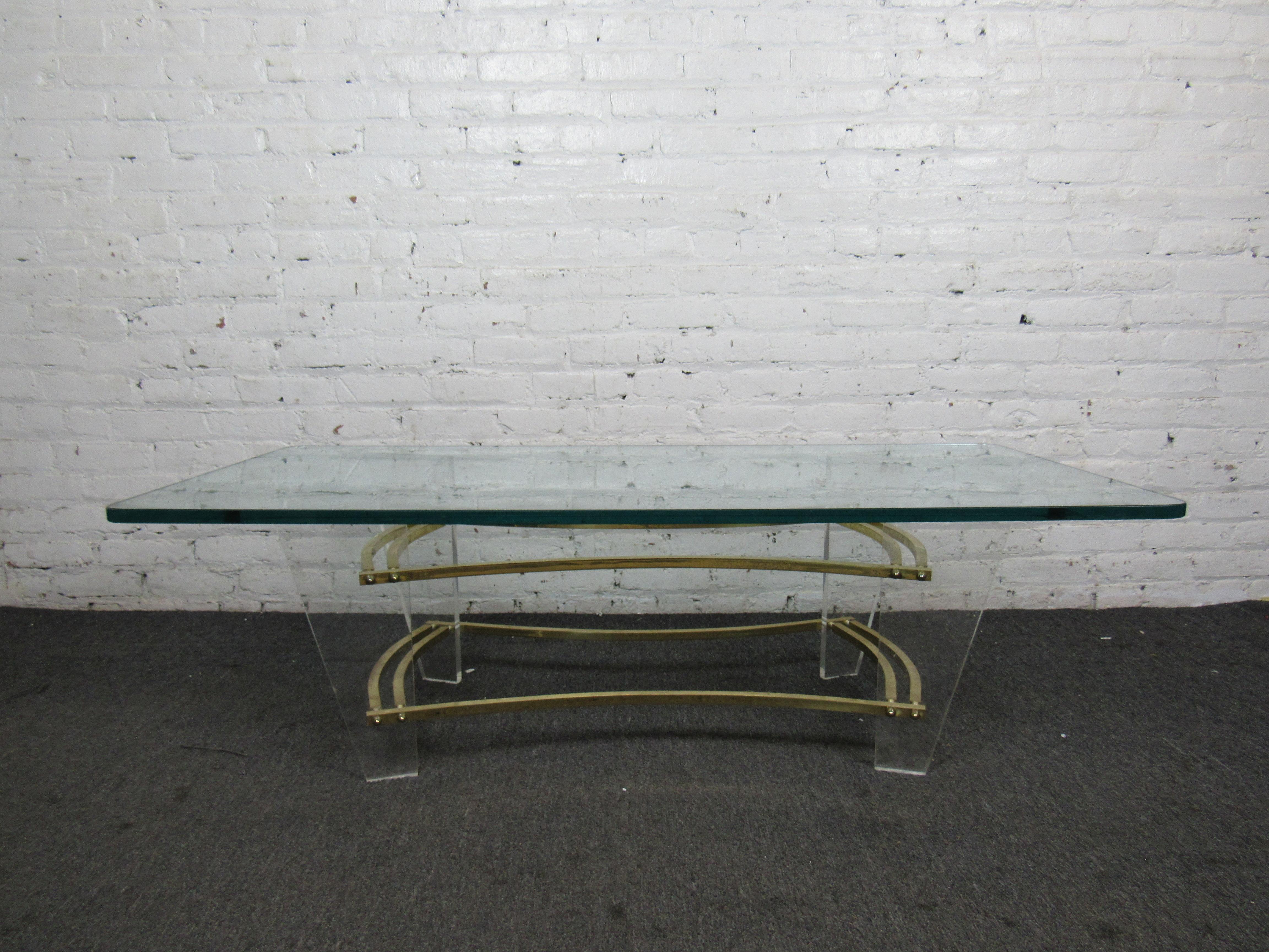 This Mid-Century Modern coffee table combines brass and lucite for a unique and interesting base, and includes a large glass top with curved edges. 
Please confirm item location with seller (NY/NJ).