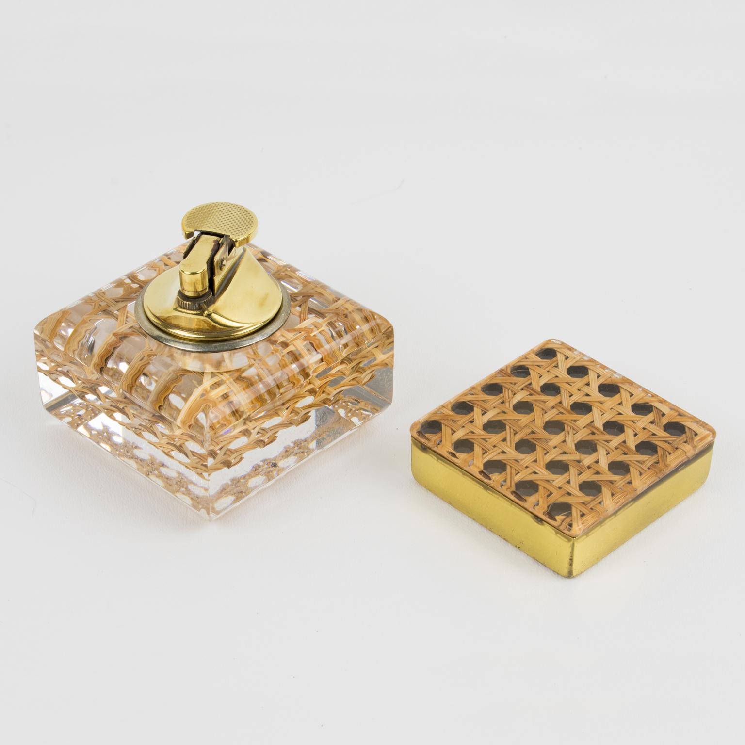 This stunning smoking set features a lighter and a box in crystal clear Lucite with real cane-work or rattan inclusions and was manufactured in the 1970s. The tobacco accessory set comprises a gaslighter and a square-shaped box for matches. The