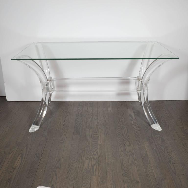 A Mid-Century Modernist Lucite saber leg console table with glass top in the style of Charles Hollis Jones. Two pairs of cylindrical, curved saber-style legs are connected by a Lucite cross-support. A rectangular glass top with a soft-polished edge