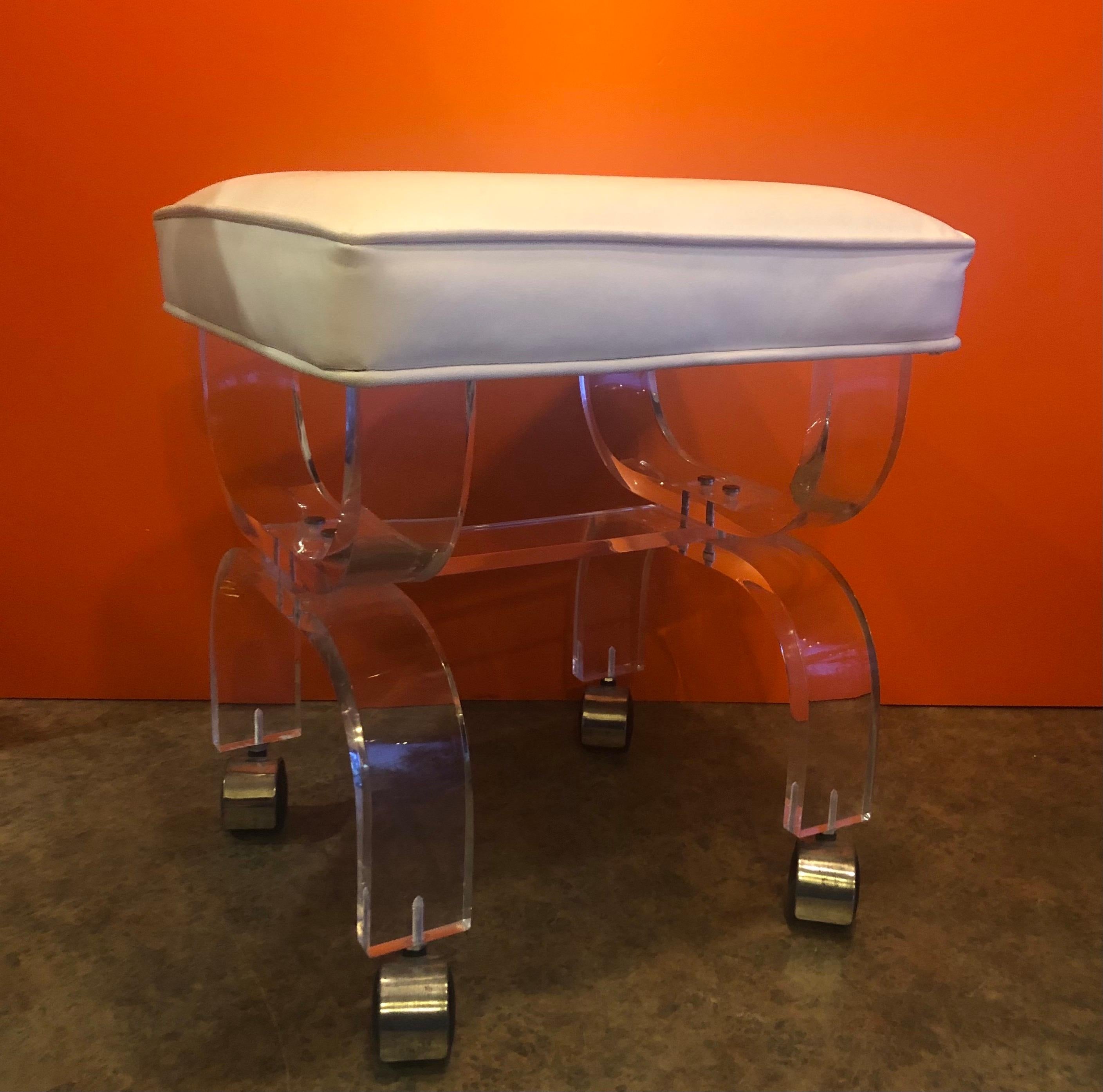Midcentury Lucite vanity stool or bench with white naughahyde seat, circa 1970s. The bench is on casters and is in good vintage condition; very solid and stabile. #1393.