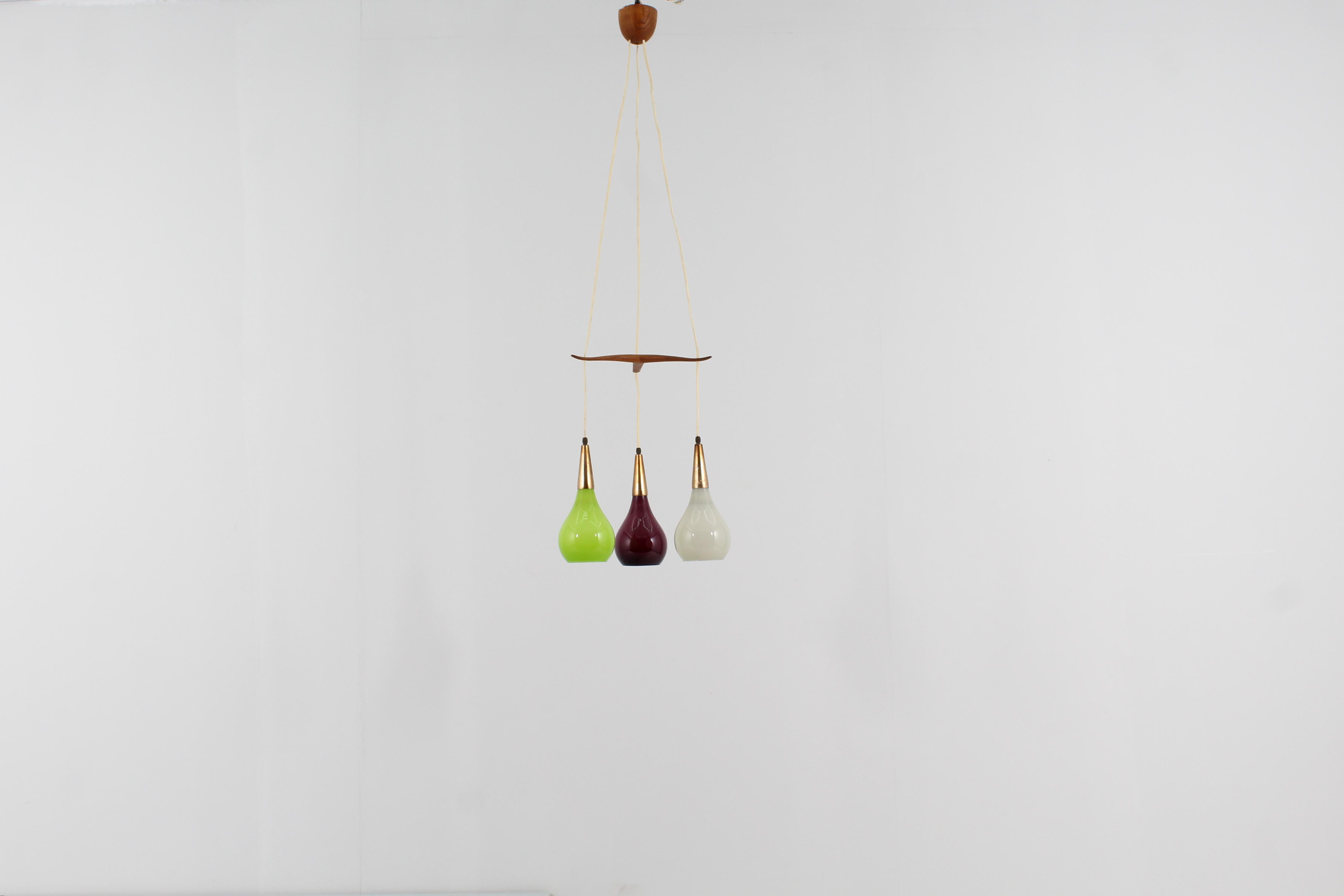 Elegant pendant lamp with three lights with wires spaced by a three-pointed element in bevelled wood and drop-shaped diffusers in green, plum and white colored glass, with brass elements. Luxus Vittsjo production label on the wood, Sweden