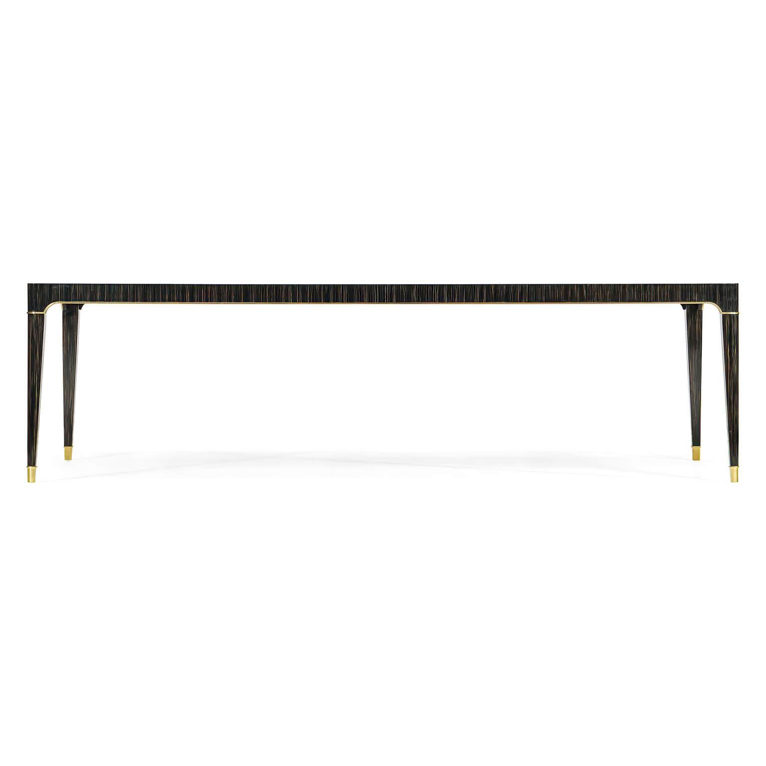 An elegant Mid-Century Modern style dining table that seats up to 10 people. With highly polished Macassar veneers, a satin brass inset center to the top, with brass trim to the apron and brass caps to the tapered legs. 

Dimensions: 108