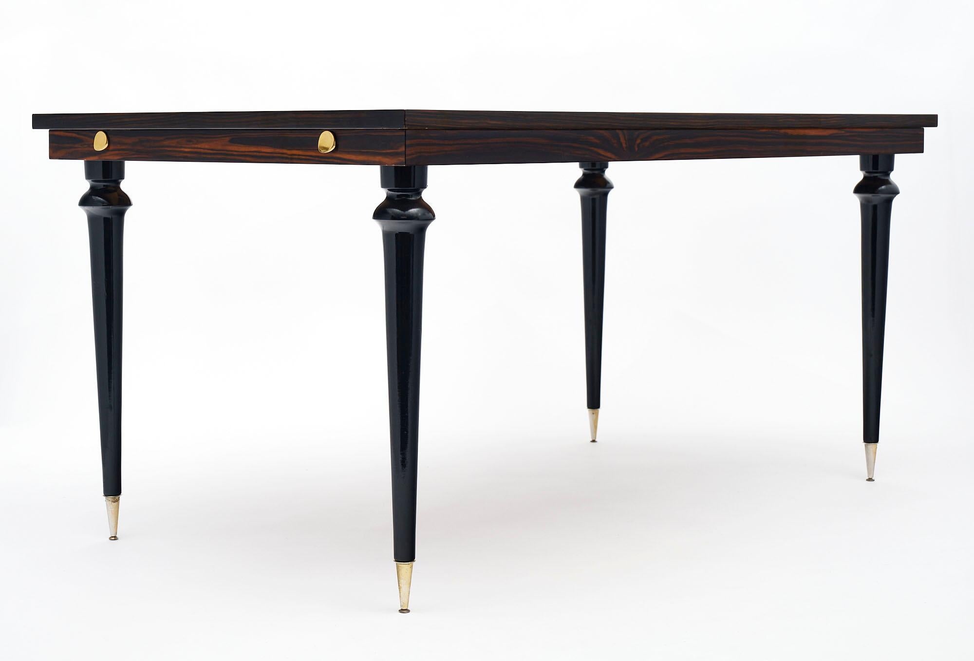 Dining table from France made with a distinct Macassar of Ebony wood veneer and striking parquetry including lemon wood inlay. The legs are tapered and capped with brass feet. Each side has pulls that enable leaves to be added for additional