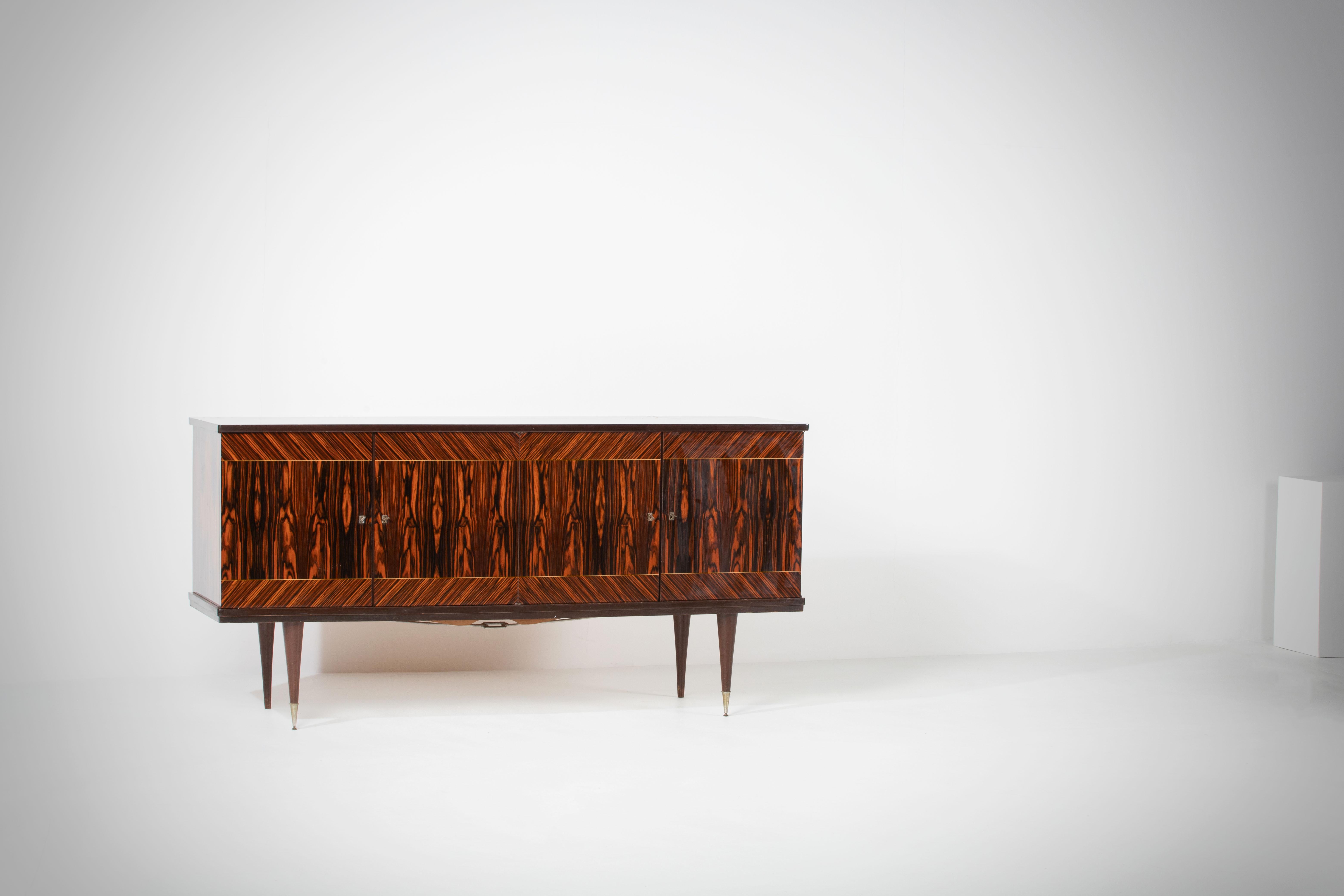 French Art Deco sideboard, credenza, with bar cabinet. 
The sideboard features stunning Macassar wood grain and rich pattern. It offers ample storage, with shelves.
The case rests on tall tapered legs with brass details. 
A unique blend of Art Deco