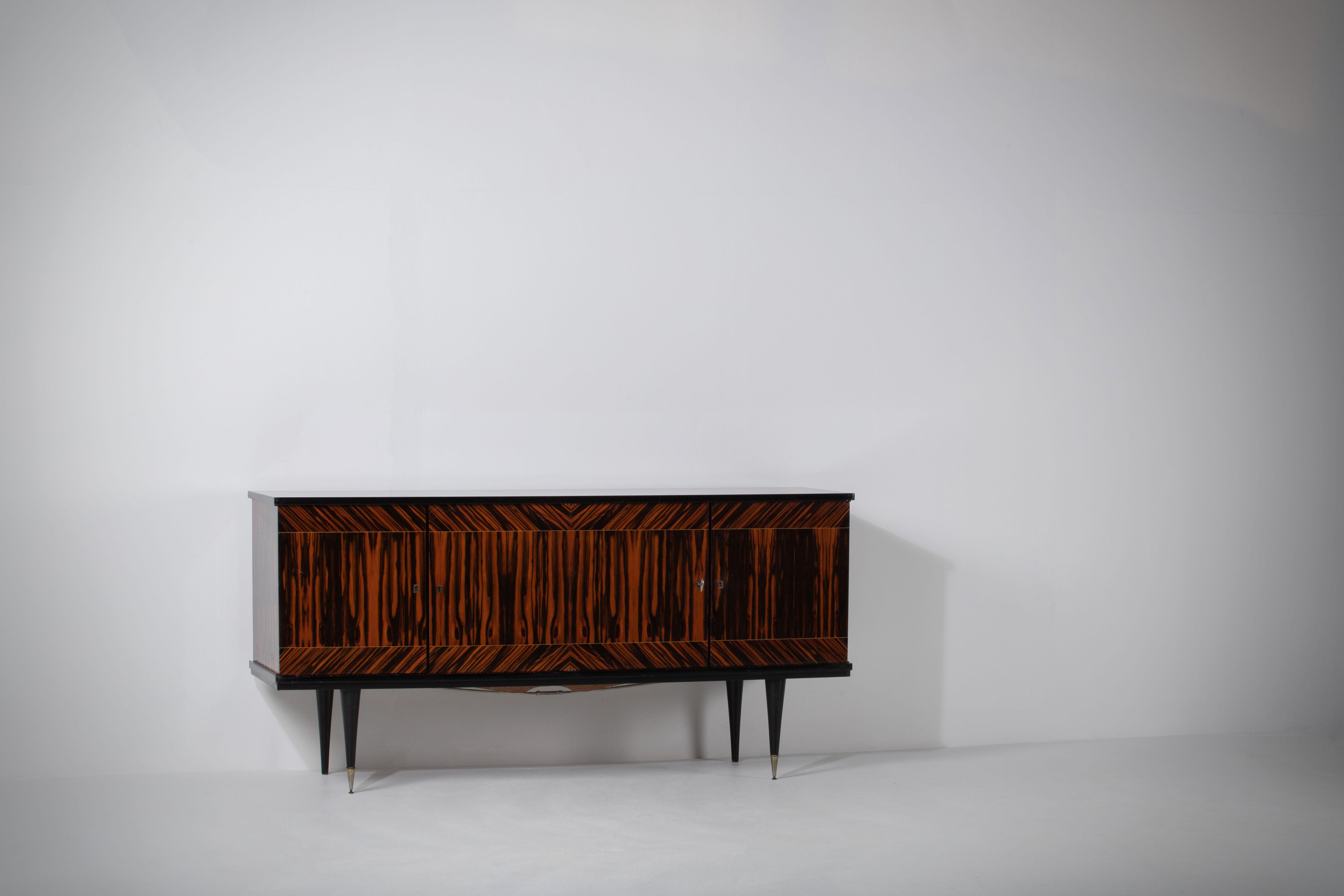 French Art Deco sideboard, credenza, with bar cabinet. 
The sideboard features stunning Macassar wood grain and rich pattern. It offers ample storage, with shelves.
The case rests on tall tapered legs with brass details. 
A unique blend of Art