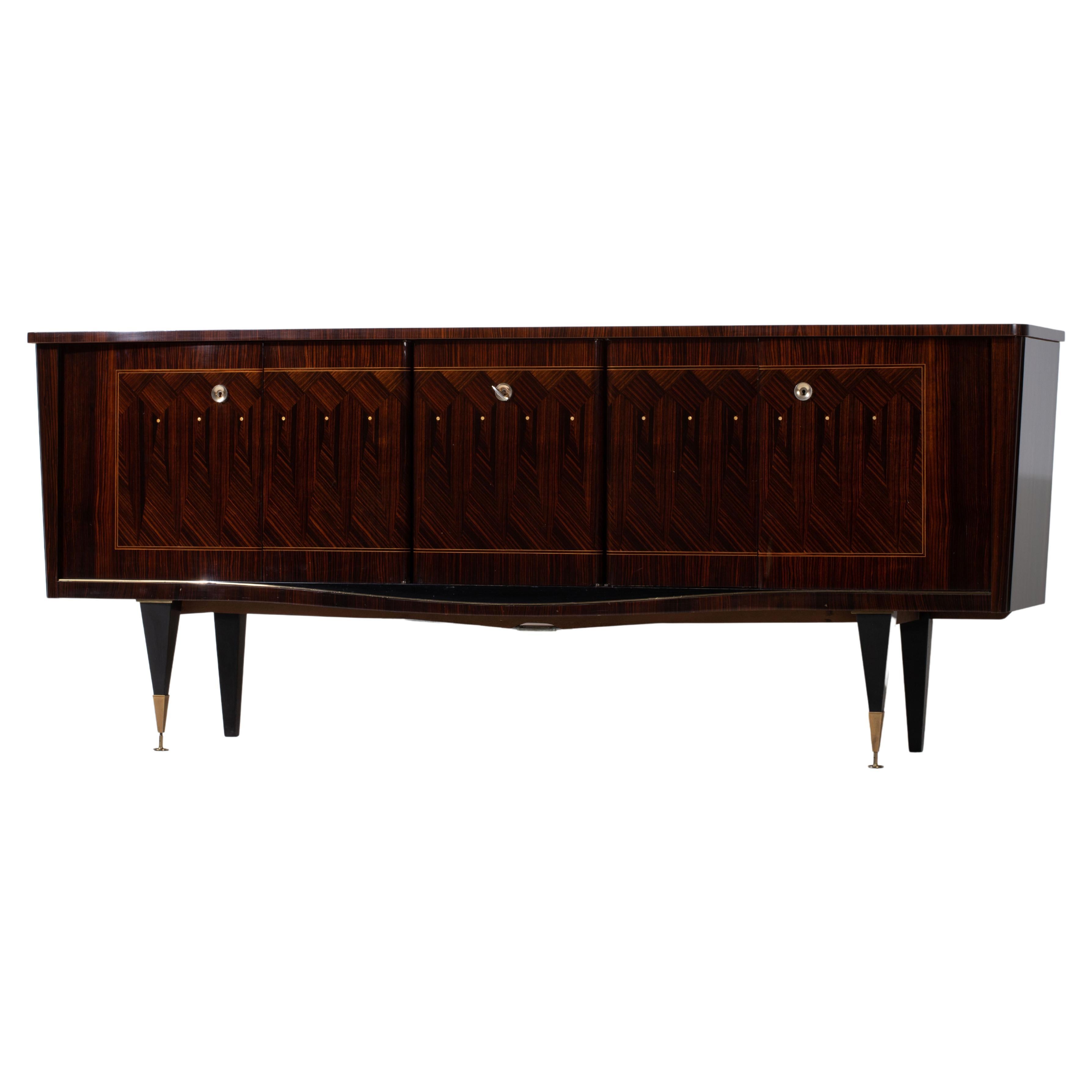 French Art Deco sideboard, credenza, with bar cabinet. 
The sideboard features stunning Macassar wood grain and rich pattern, mother of pearl. It offers ample storage, with shelves.
The case rests on tall tapered legs with brass details. 
A unique