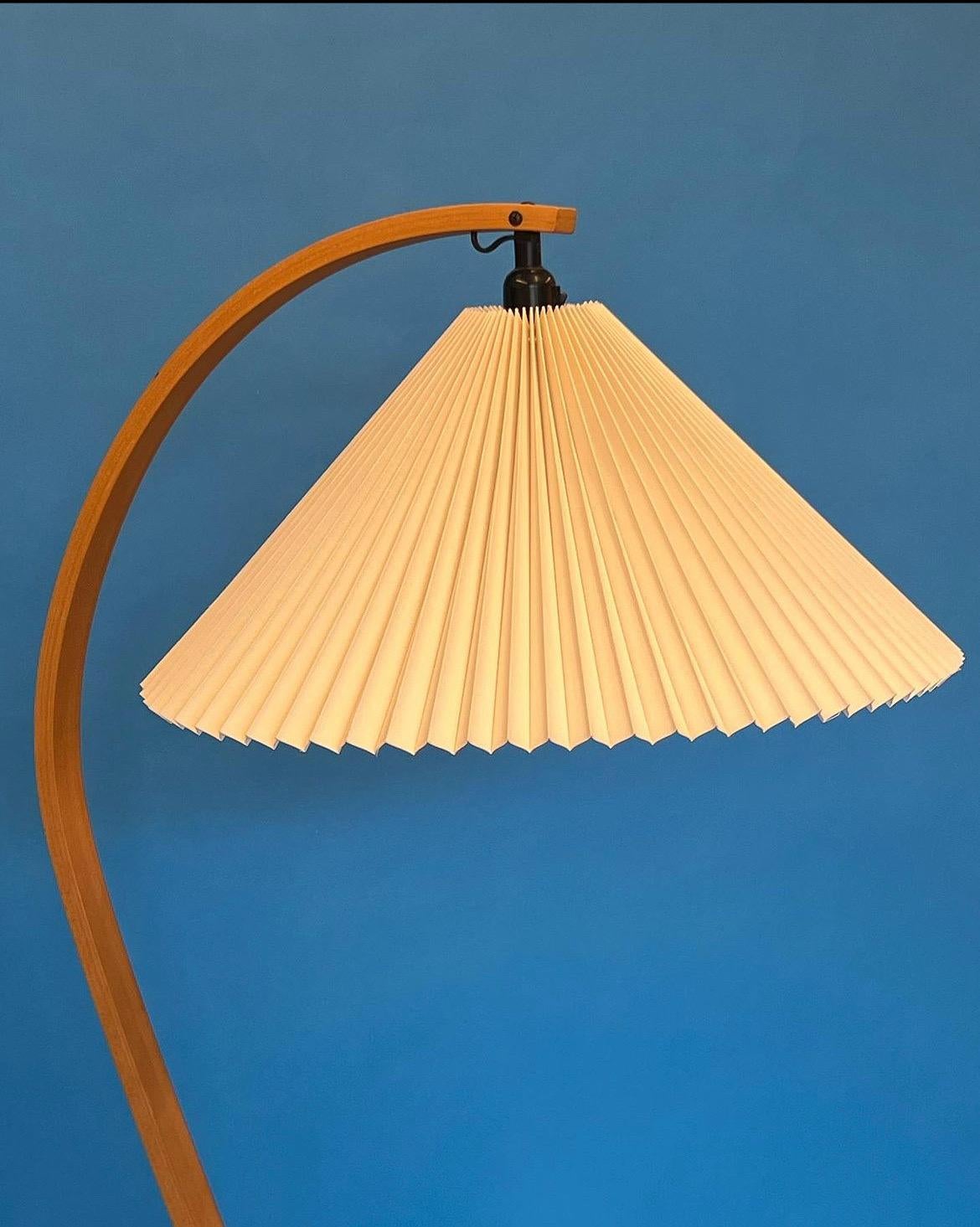 Lampadaire conçu par Caprani Light AS, vers les années 1970. La lampe présente une belle tige en bois de hêtre courbé, une base en forme de croissant en fonte et un abat-jour plissé en lin blanc cassé. La prise est équipée d'un interrupteur