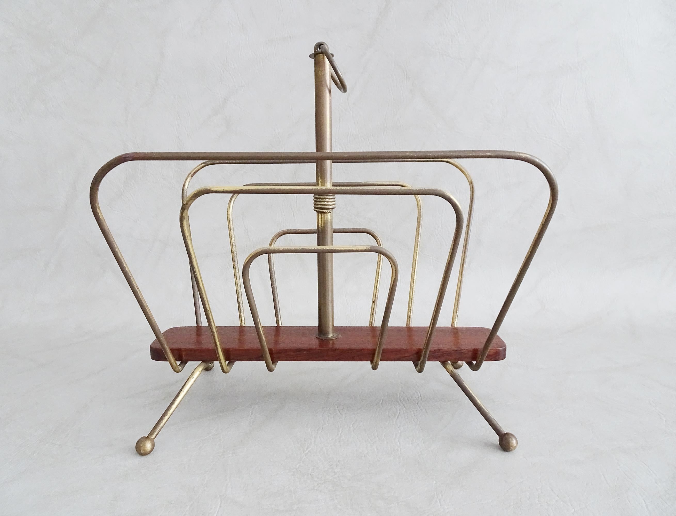 Mid century magazine rack made of brass and wood in the style of Carl Auböck. Sculptural minimalist design made of bent brass rods. Particularly characteristic is the raised stick with a brass ring as a handle, as well as the ball feet. These