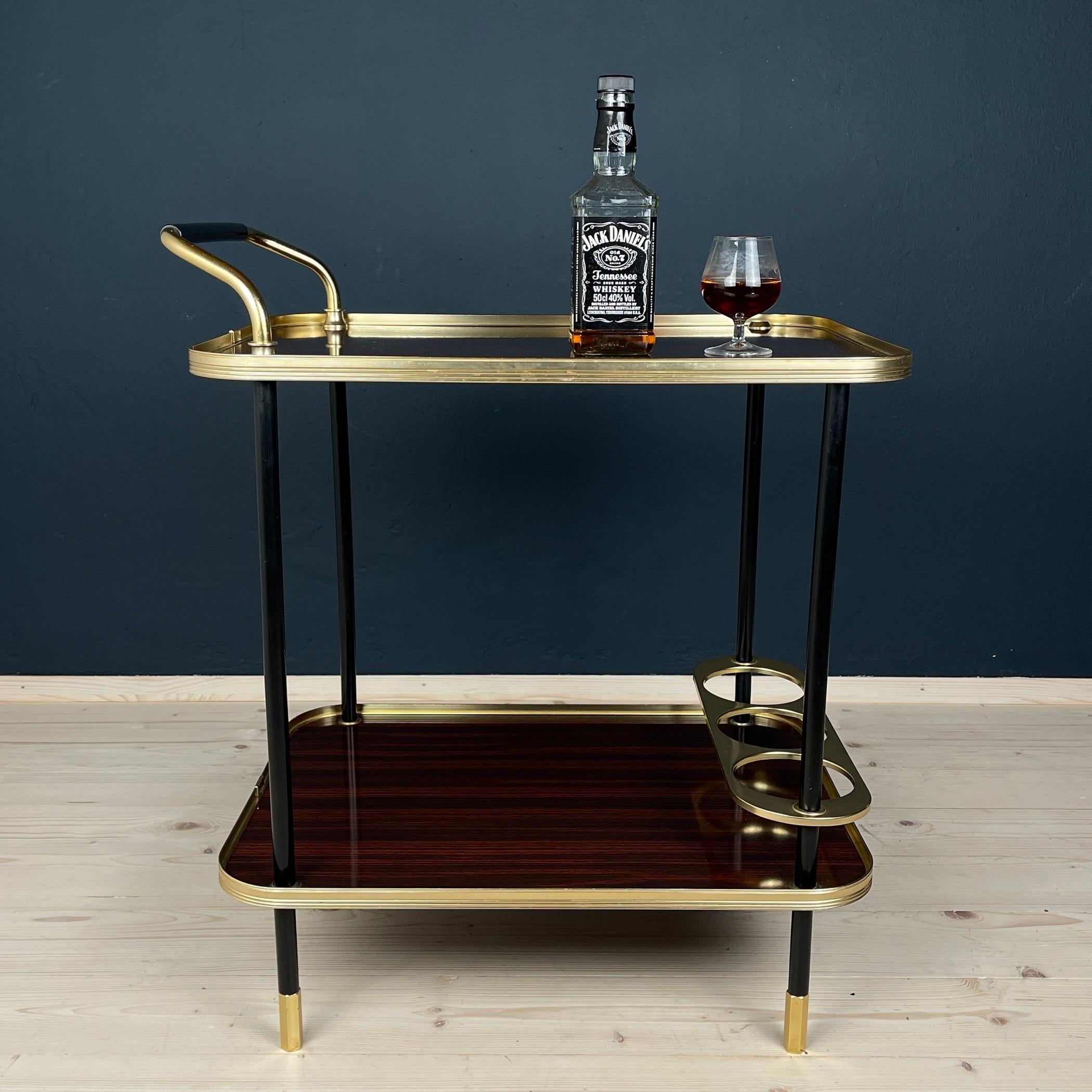 Behold the exquisite bottle trolley, a masterpiece designed in Italy by Ico and Luisa Parisi for Mb Italia in the glamorous era of the 1960s. This creation is a captivating fusion of materials, seamlessly blending Formica, aluminum, and gold metal