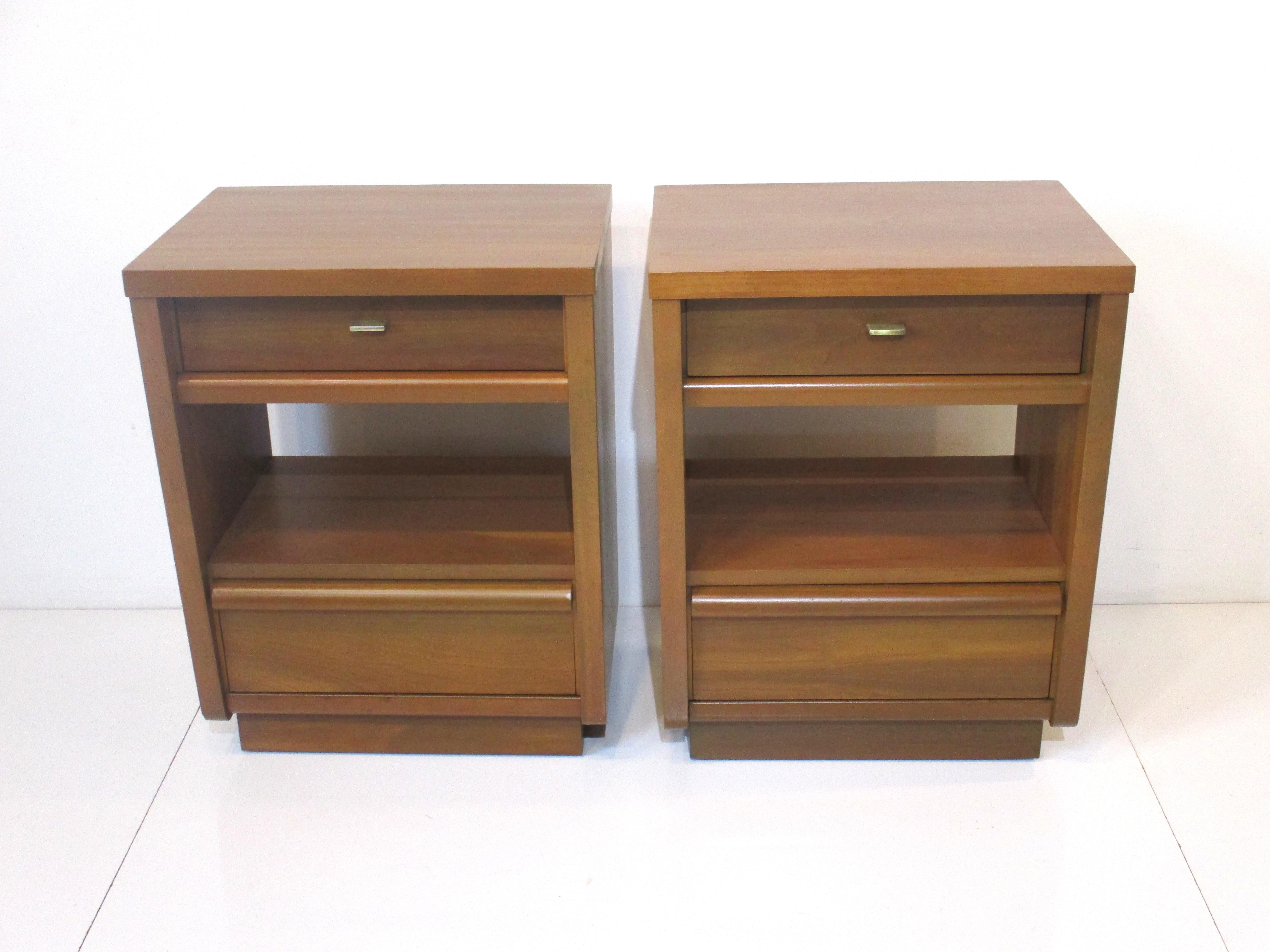 A pair of medium mahogany mid century nightstands with upper and lower drawers and storage to the mid section . A thin brass pull and tapered sides give the piece great style and a lighter feel designed and made in the manner of the Widdicomb