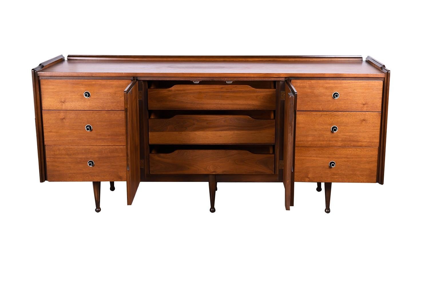 Stunning walnut Mid-Century Modern credenza, dresser for Mainline by Hooker Furniture Company circa 1960’s. This unit features a rectangle top with sculpted raised backsplash and side edges above a whopping 9 drawers. Three deep spacious drawers