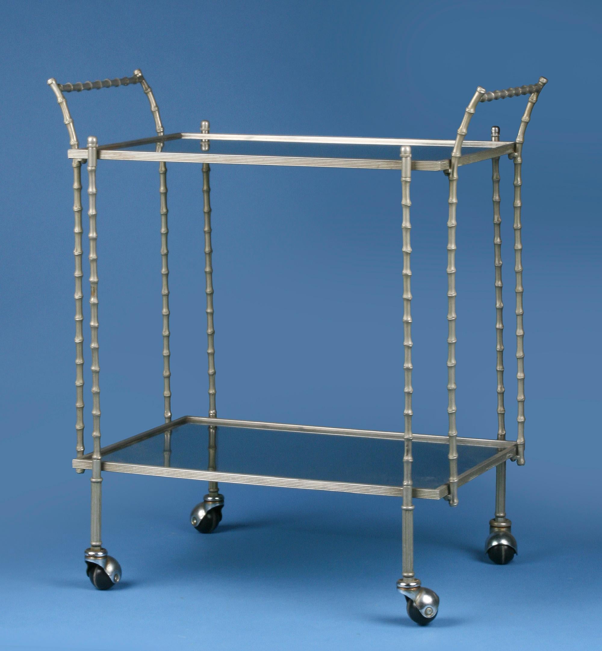 A two tiered bar cart / tea trolley by Maison Baguès Paris. Stylish and elegant. The faux bamboo frame is made of nickel-plated bronze. Inside two brown smoked glasses shelfs. The cart is easy to roll. The wheels function well.
Maison Baguès was