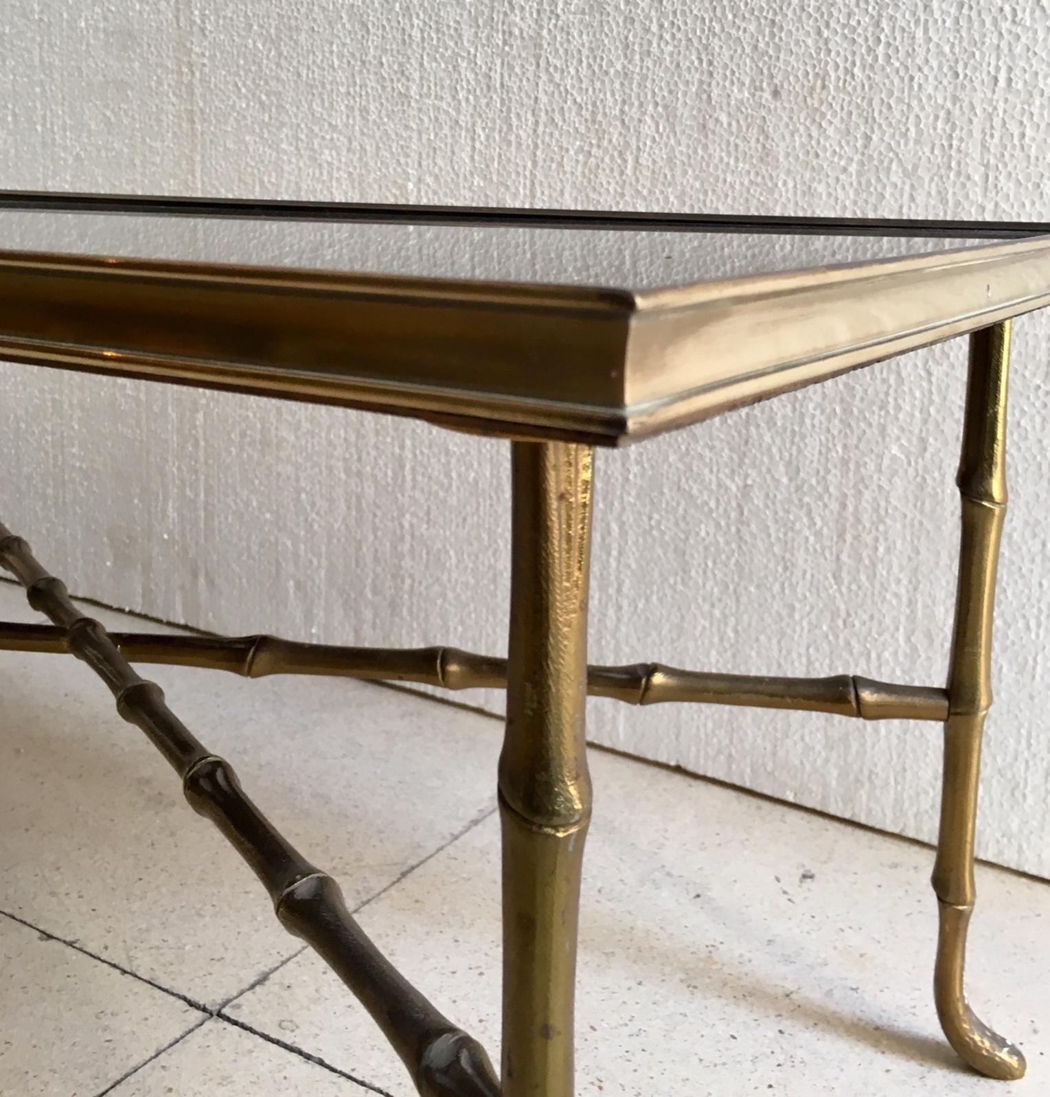 A coffee table, in the manner of French designer Maison Bague`s, with brass faux bamboo frame, inset with black mirrored glass top, above a cross beam stretcher.