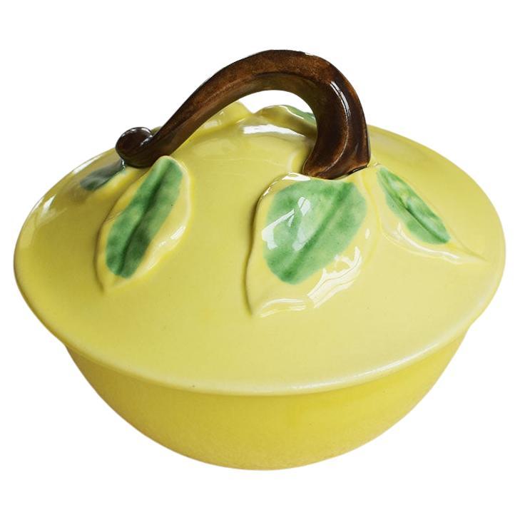 A set of majolica fruit motif plates and matching compote with lid. Glazed in yellow and green, this set includes four ceramic pear or lemon motif side plates or dishes, and one large compote with lid and handle. Each dish is shaped as a set of