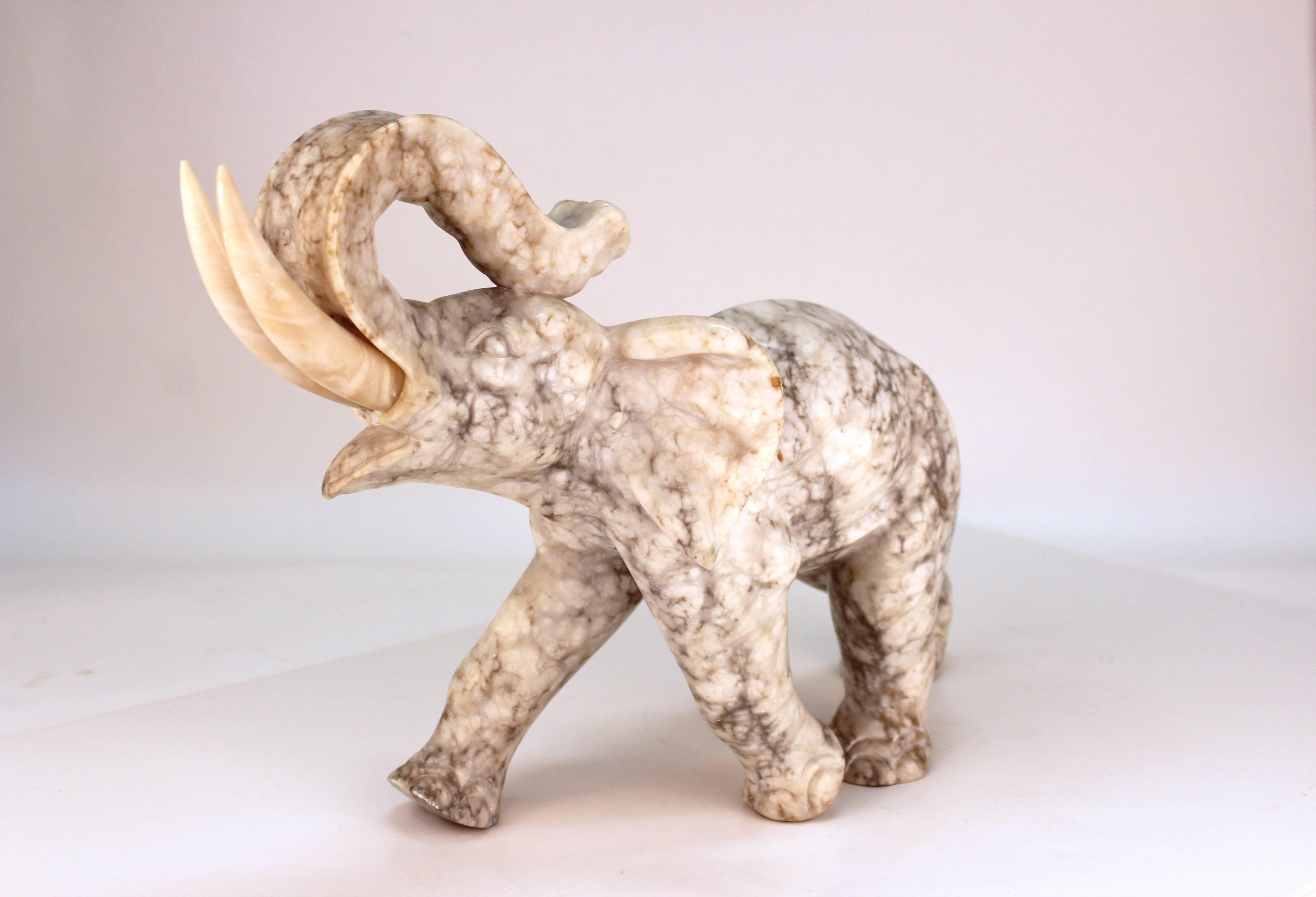 A Mid-Century Modern elephant figure carved in marble, with tusks made of alabaster. Both tusks are removable. One tusk had screw end restored. Breaks and cracks to both tusk insert holes. Small chip on back of elephant ear.