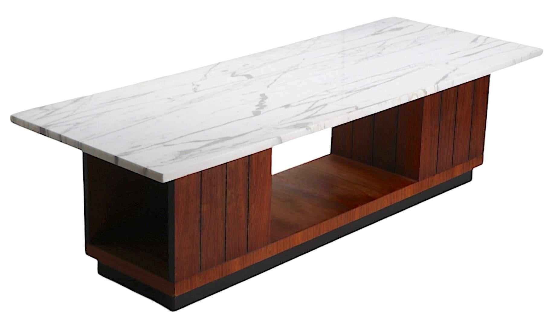 Classic Mid Century Modern architectural coffee table having a thick rectangular top which rests on a wood base. The base features two opposing block form cabinets, each having an open  bookcase storage space, with a rectangular plinth bottom. The