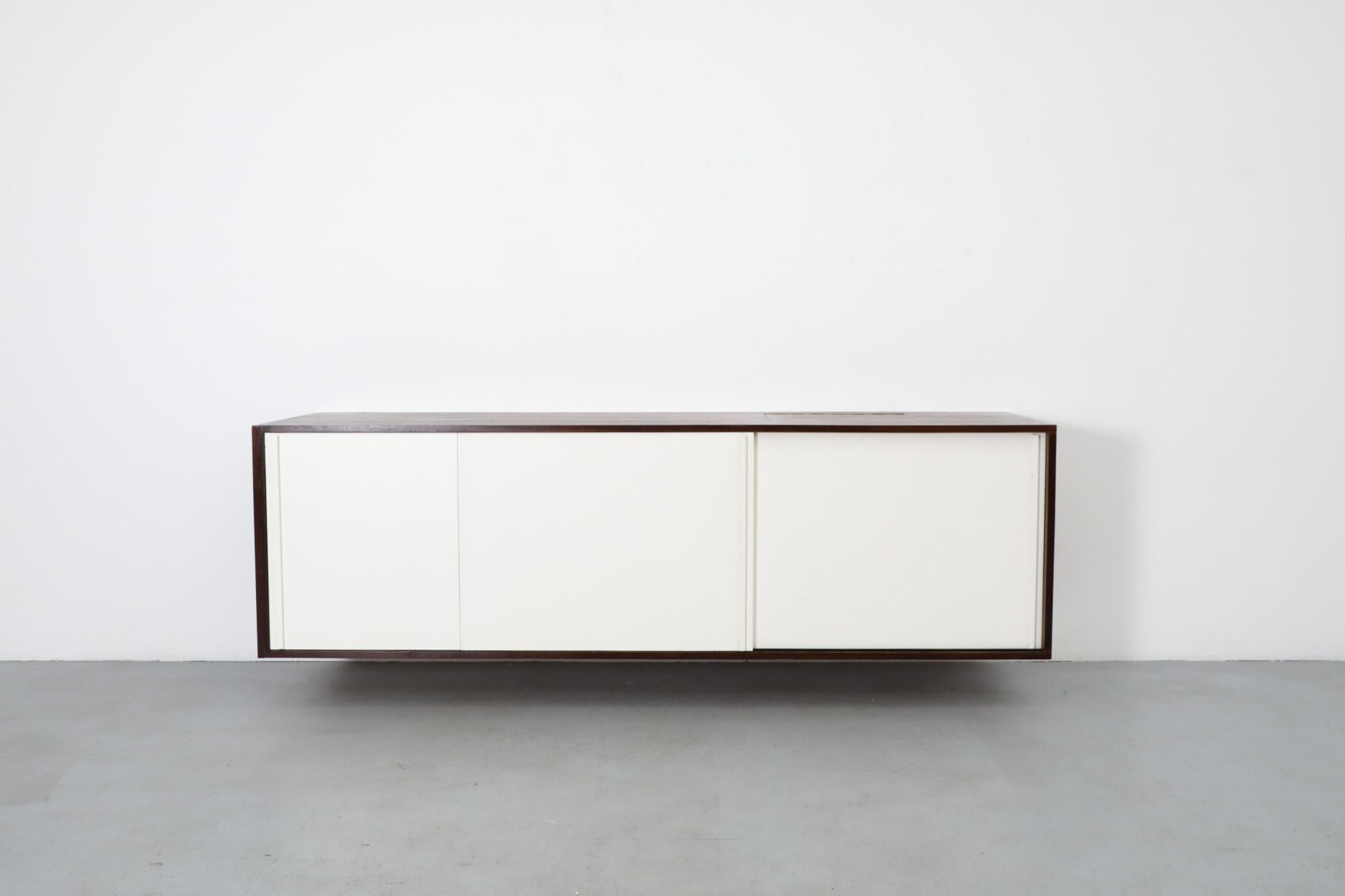 Dutch Mid-Century floating wall mount credenza by the iconic and innovative designer Martin Visser. This gorgeously designed piece features a hidden record player space with a flip-top door, a handsome wenge frame, and white sliding doors that house