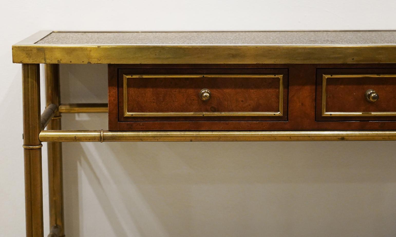This 20th century brass and burled walnut console table by Mastercraft features an etched and patinated brass panel top above brass piping framed short burled walnut drawers flanking one long drawer all supported within a stylized ringed bamboo