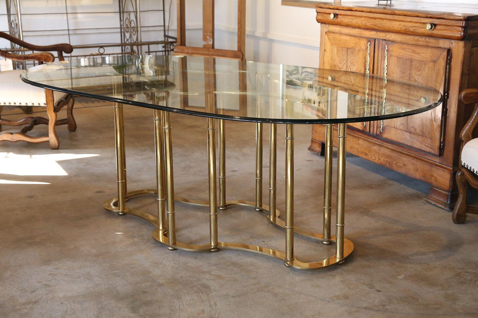 Beautiful brass Mastercraft dining table with original oval beveled glass top. The brass base consists of 12 vertical supports with a flat racetrack top and bottom supported on 12 bun feet. The original beveled glass top has light scratch markings