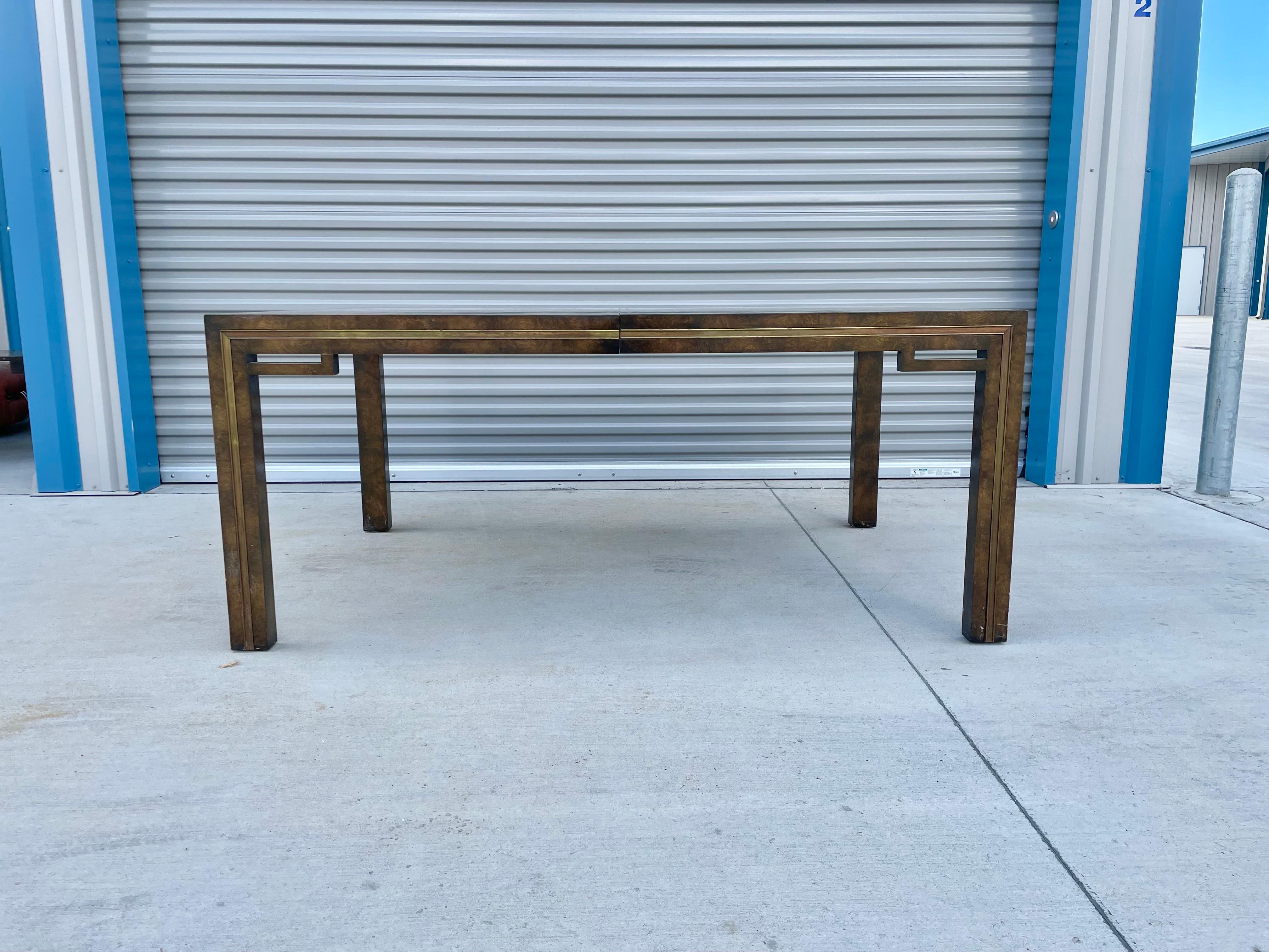 Midcentury burlwood dining table designed by William Doezema and manufactured by Mastercraft in the United States circa 1970s. This beautiful dining table features a burlwood frame with a brass strip around the table. The dining table also has two