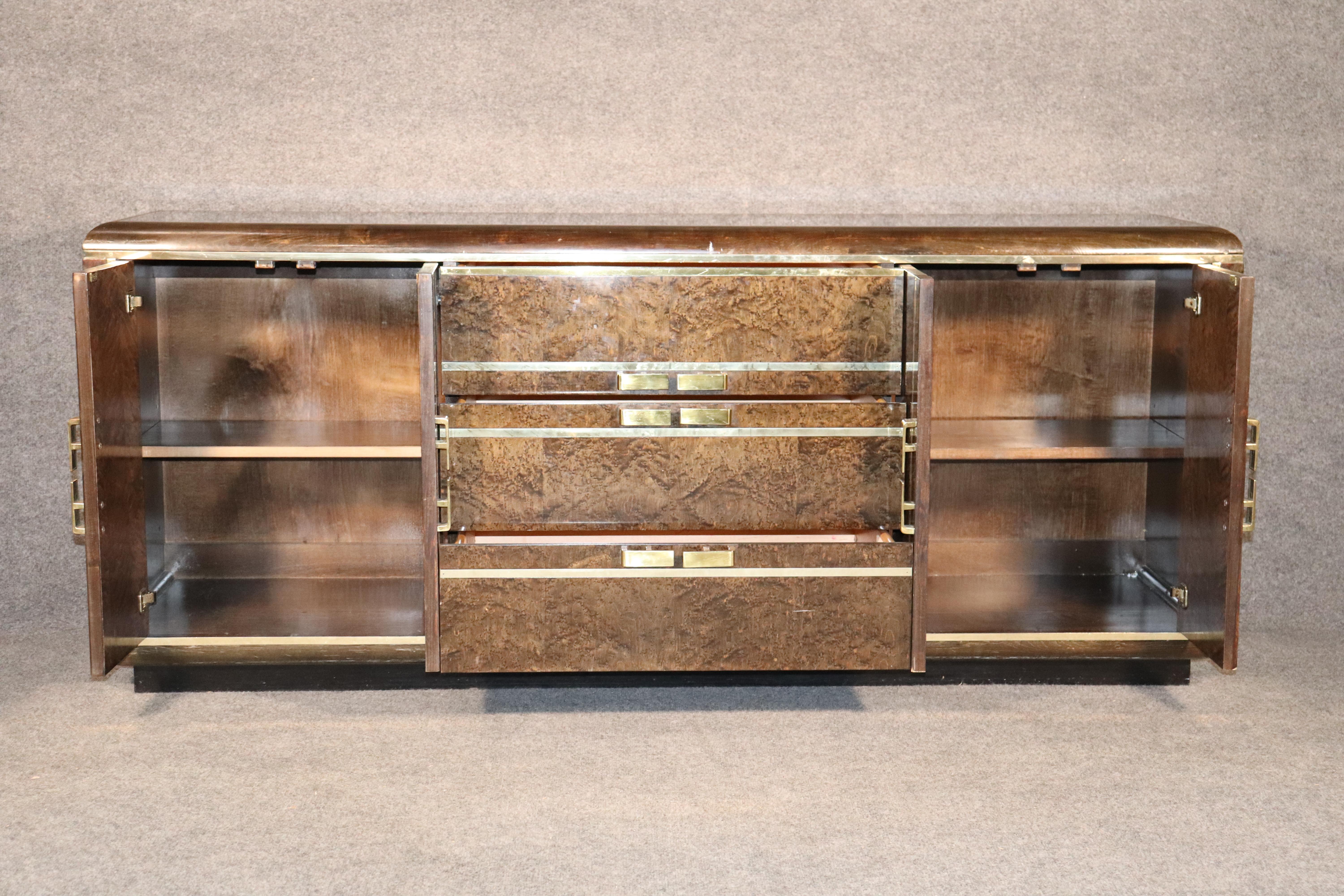 Long dresser in deep burl veneer with accenting brass trim and hardware. Three wide drawers and two side cabinets give ample storage.
Please confirm location.