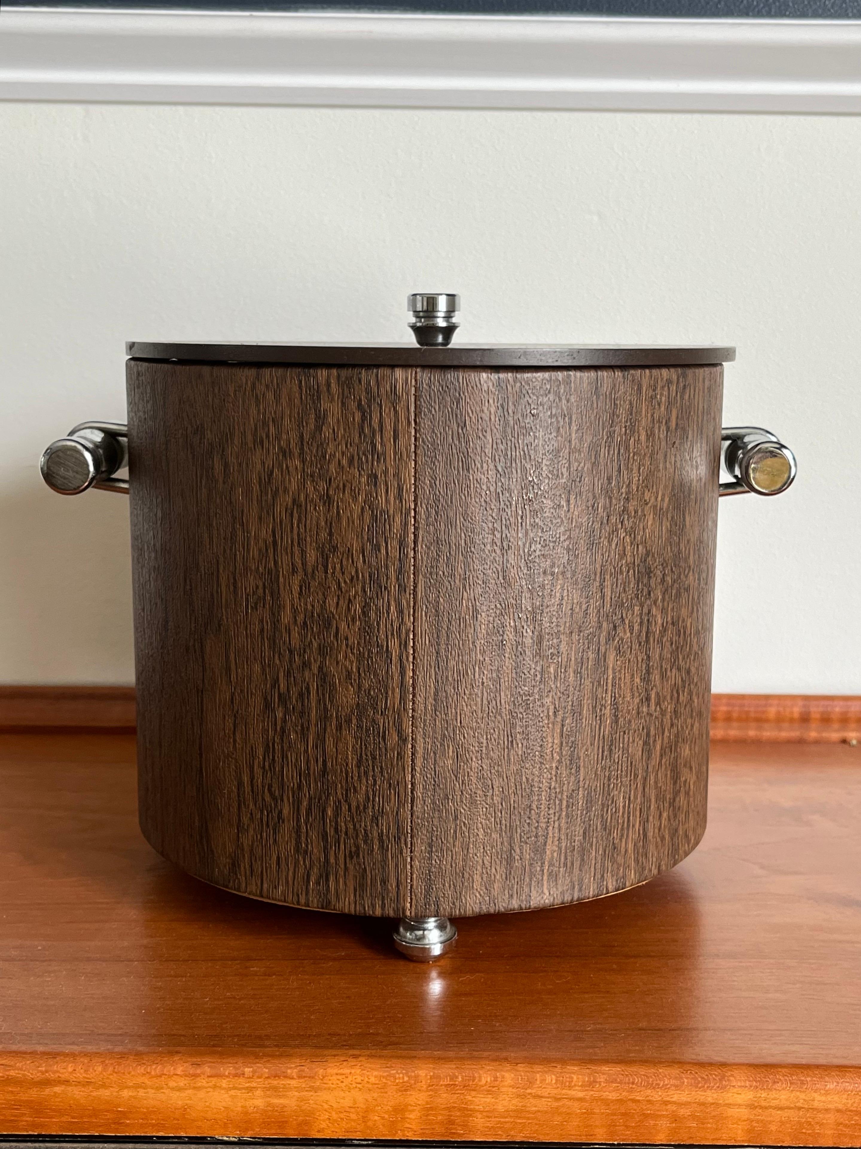A true survivor. Beautiful faux wood grain ice bucket by Maxwell Phillips. A classic look with faux wood offset with chrome bamboo handles, feet and top finial. Insulated glass interior. Maxwell Phillips style shines! Glasses are for staging and not
