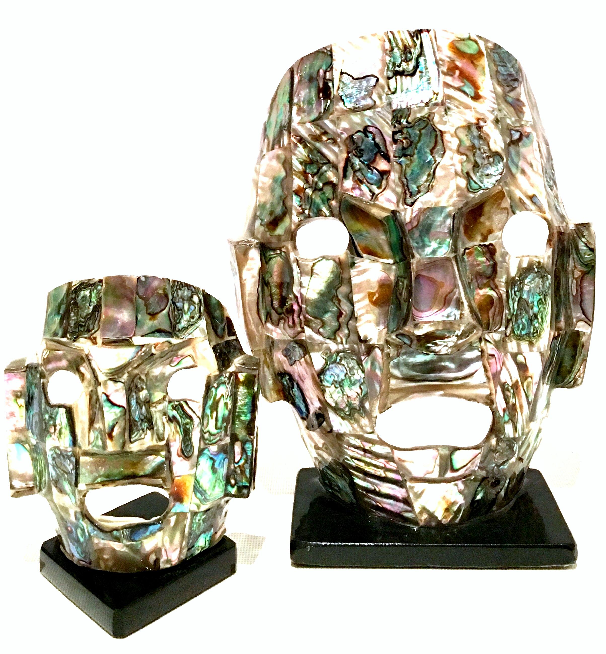 Mid-20th century Mayan style pair of mounted mosaic abalone shell ceremonial mask sculptures. This pair features two sizes. The smaller mask sculpture measures approximately, 4.25