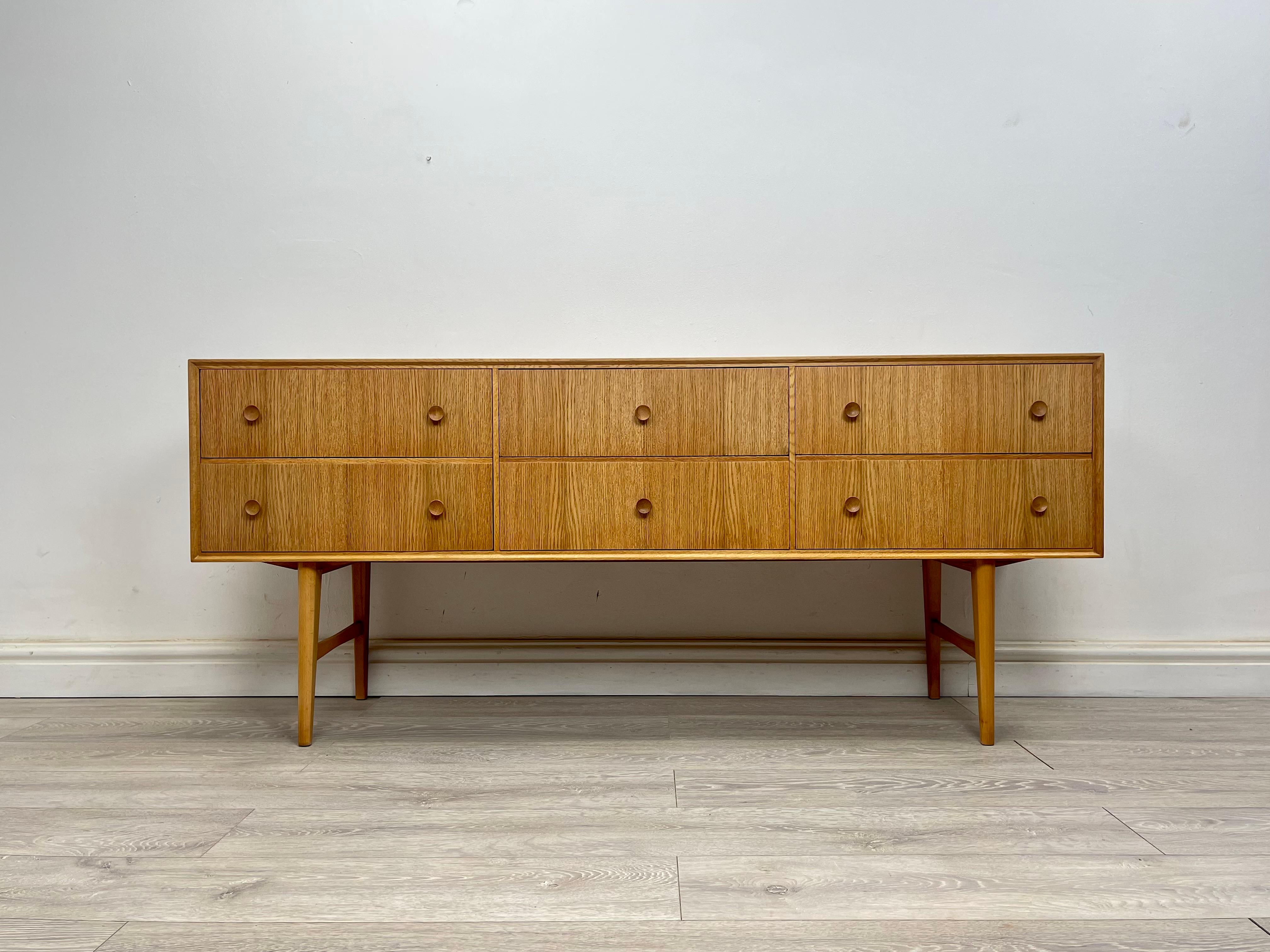 SIDEBOARD 
Stunning midcentury oak sideboard / chest of drawers made by Meredew circa 1960. The sideboard is very well made and hard to find in this model .

This model has interesting design it stands on elegant splayed legs, there’s six drawers