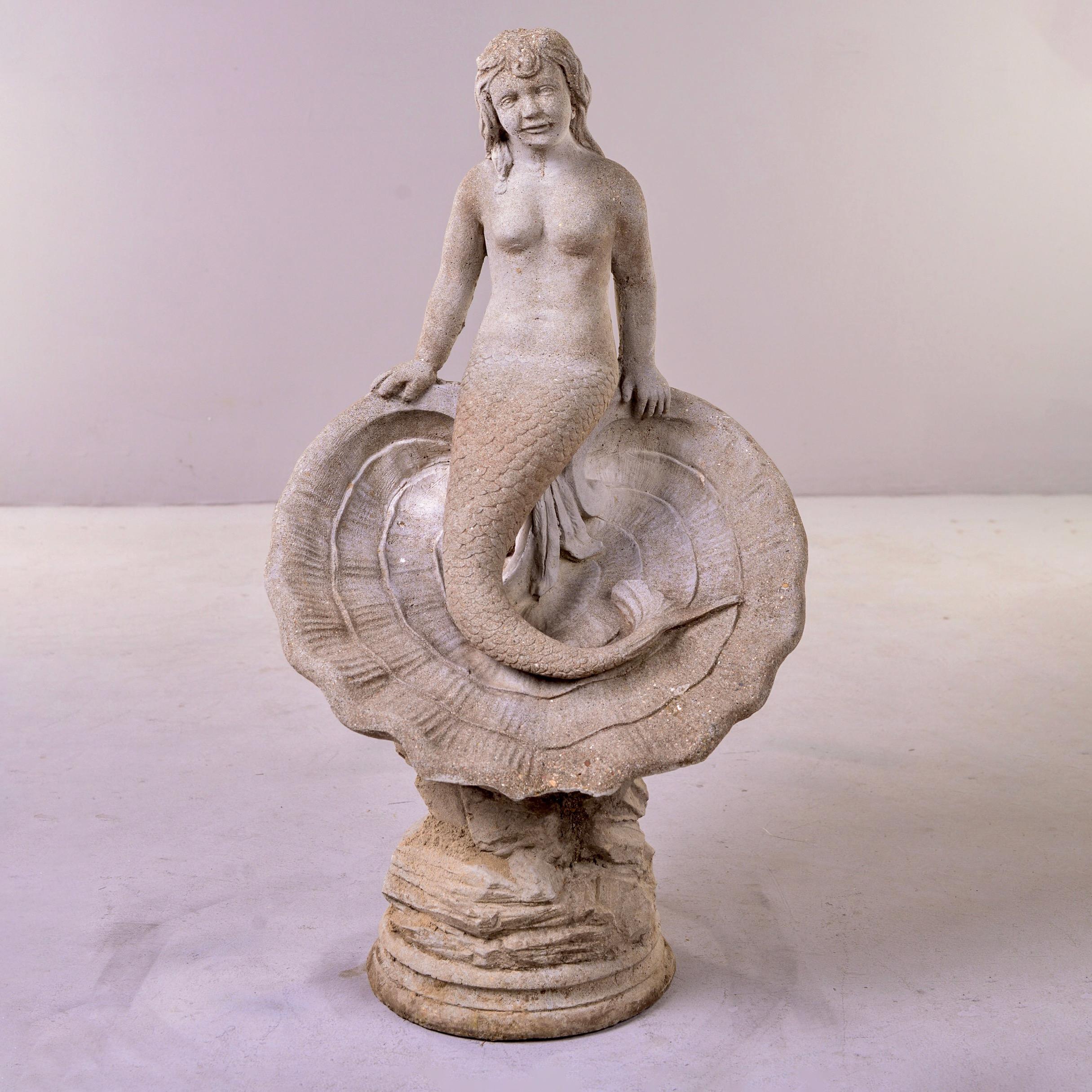 Circa 1950s garden statue of a mermaid perched on a shell. This stands over three feet tall. Some scattered age-related patina/moss to surfaces. 

One chip to scallop edge at bottom of clamshell - see last detail photo.
