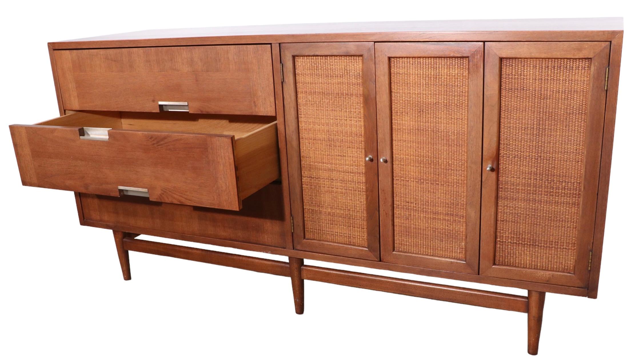 Slick and clean Mid Century dresser designed by Merton Gershun for American of Martinsville. The dresser  features a bank of three drawers, flanked by cane front doors, which open to interior drawers, and open storage space. This example is in very