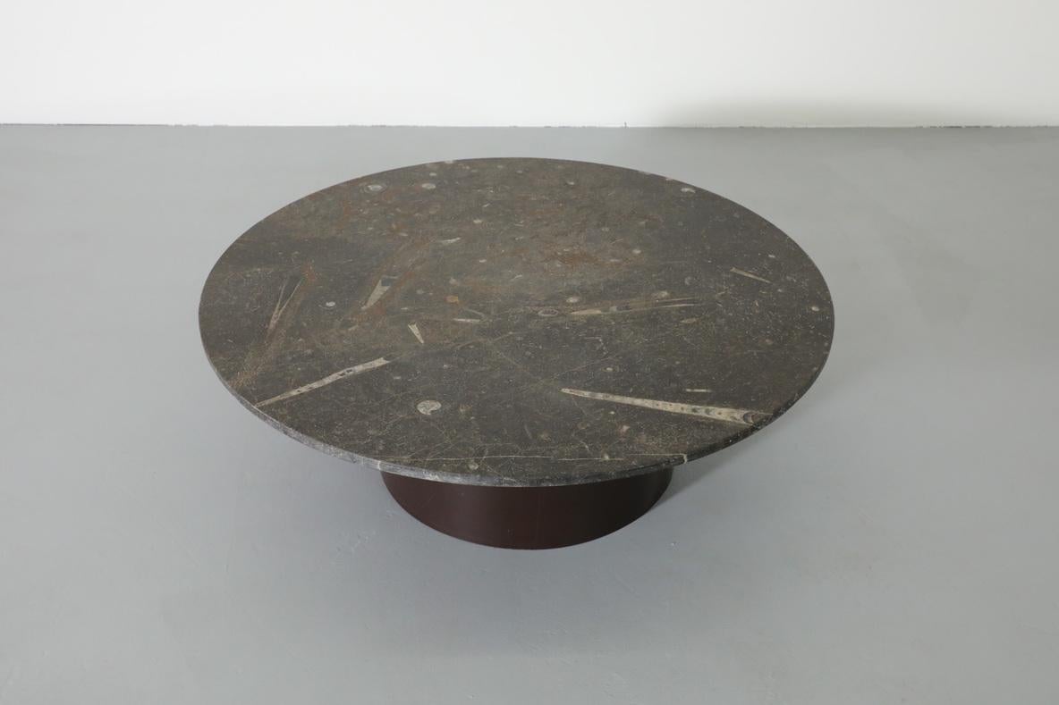 Stunning Metaform style round fossil stone coffee table with brown enameled metal pedestal base. Beautiful array of fossilized sea shells embedded in stone top. In good original condition with some wear to the enamel on the base. Wear is consistent
